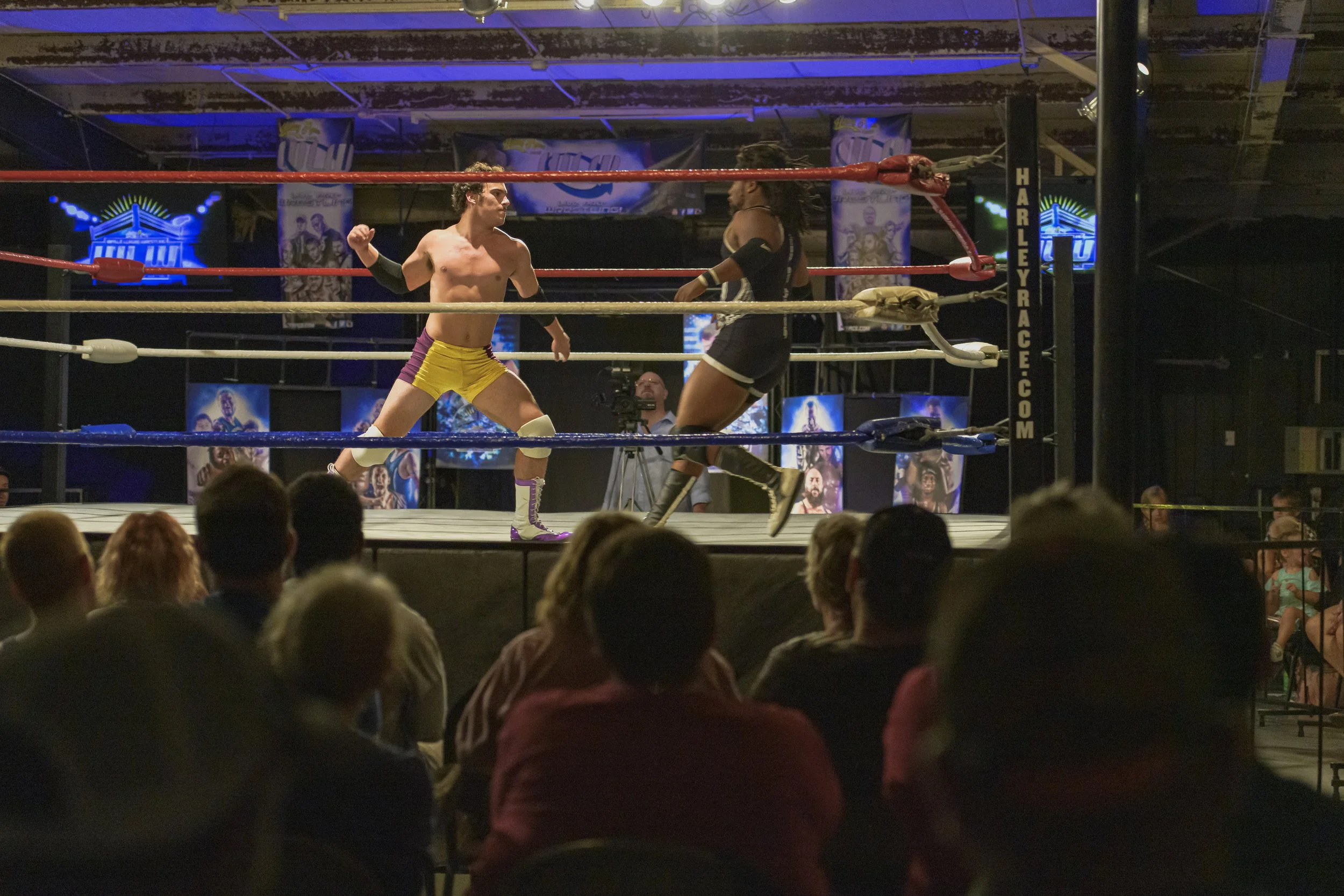 Two wrestlers face each other near the ropes as the audience watches at the 2022 World League Wrestling event.