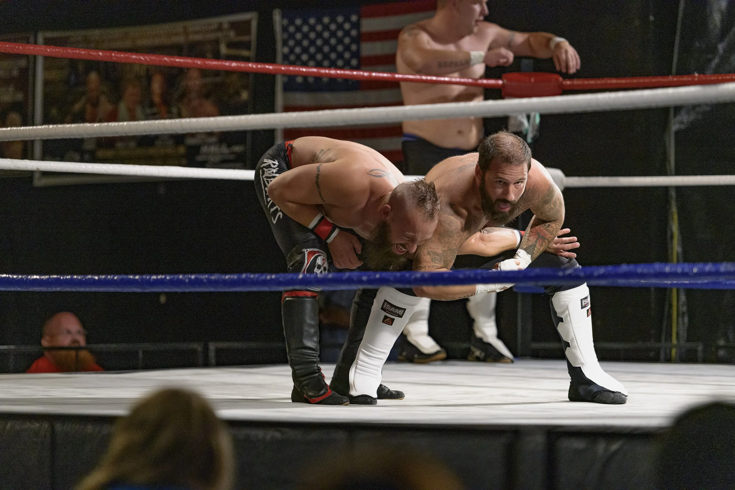 Two wrestlers grapple near the ropes while another waits at the ring edge at the 2022 World League Wrestling event.