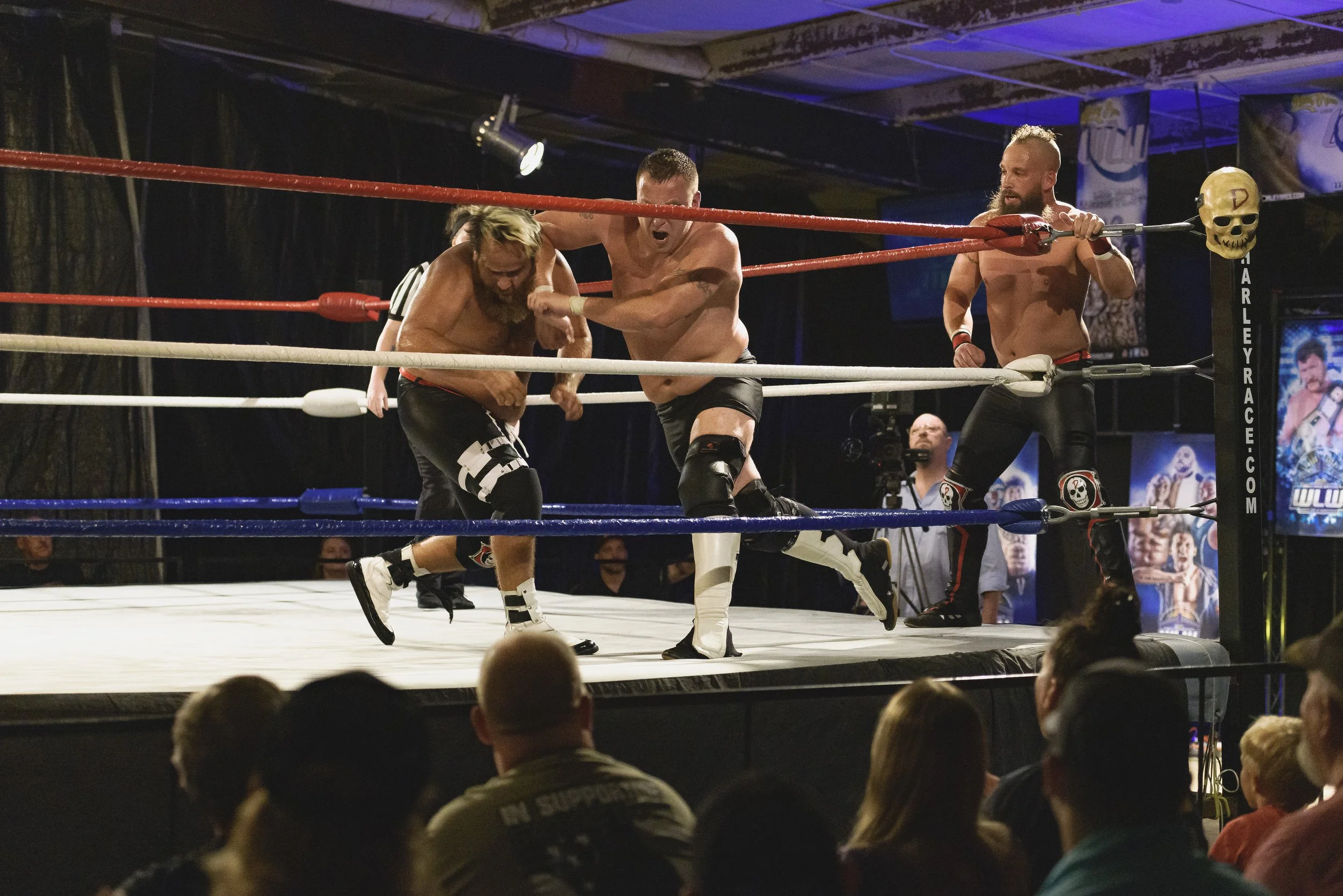 Two wrestlers struggle beside the ropes while another waits in the corner at the 2022 World League Wrestling event.