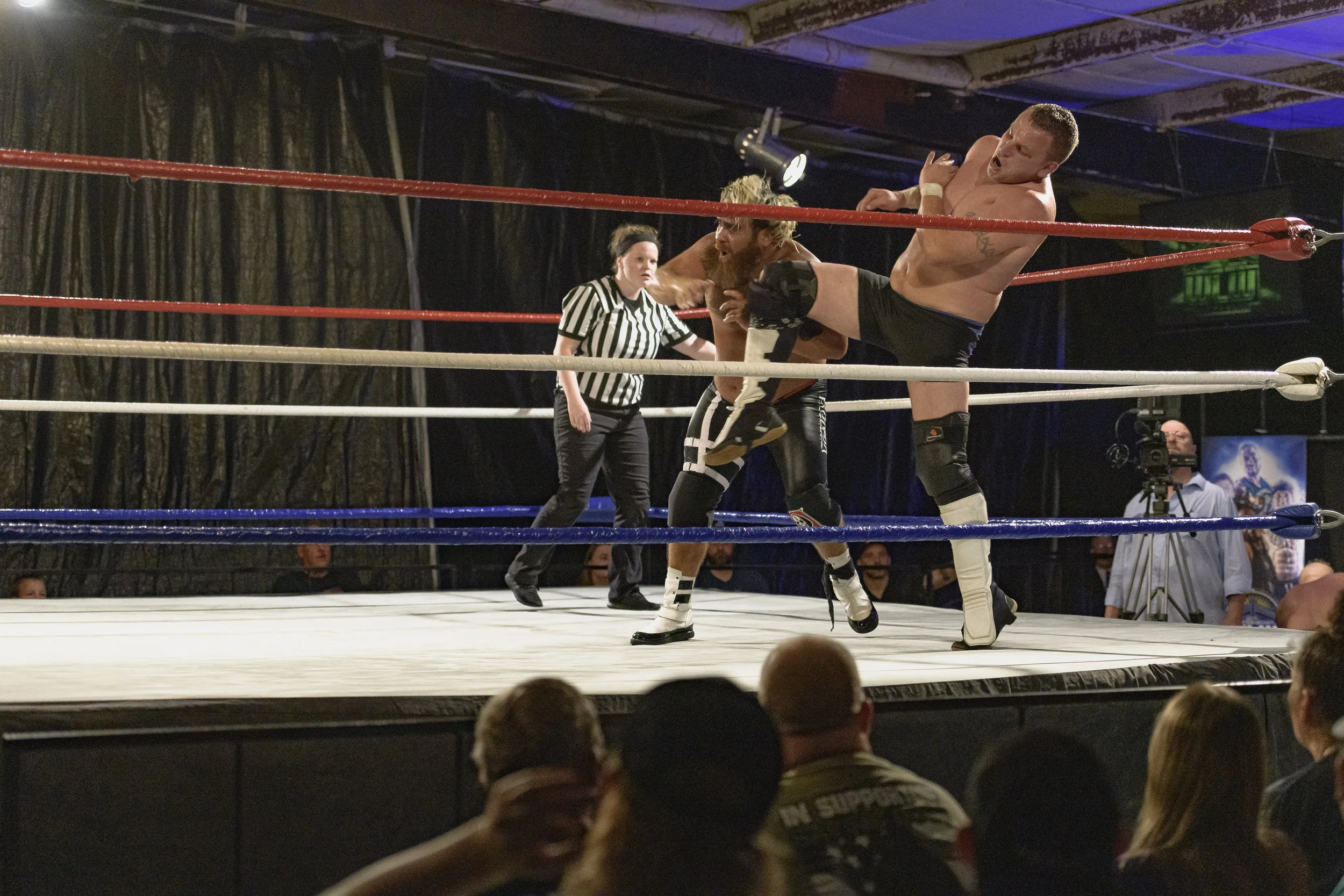 A wrestler raises a knee toward an opponent as the referee watches at the 2022 World League Wrestling event.