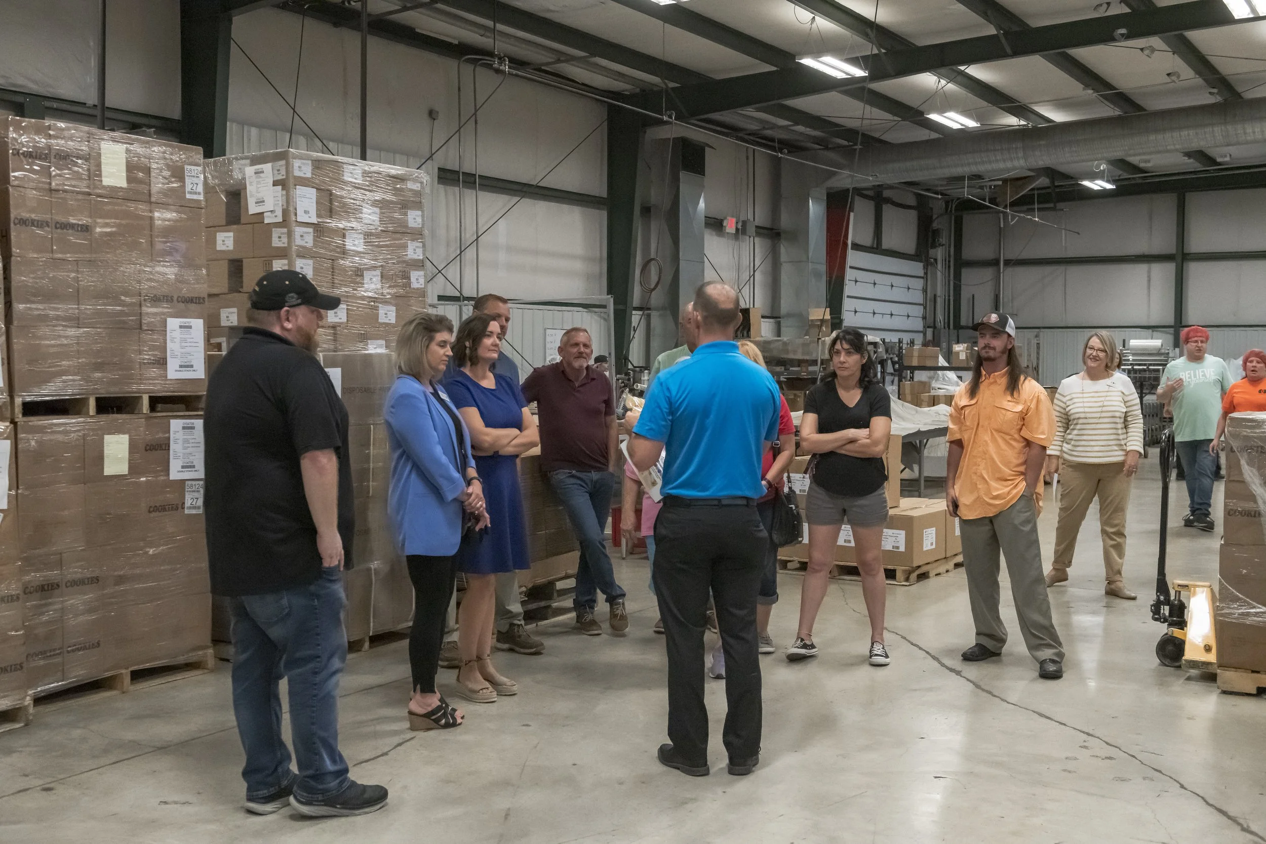 Visitors gather beside stacked pallets of boxes during a facility tour at the 2022 BCI Open House.