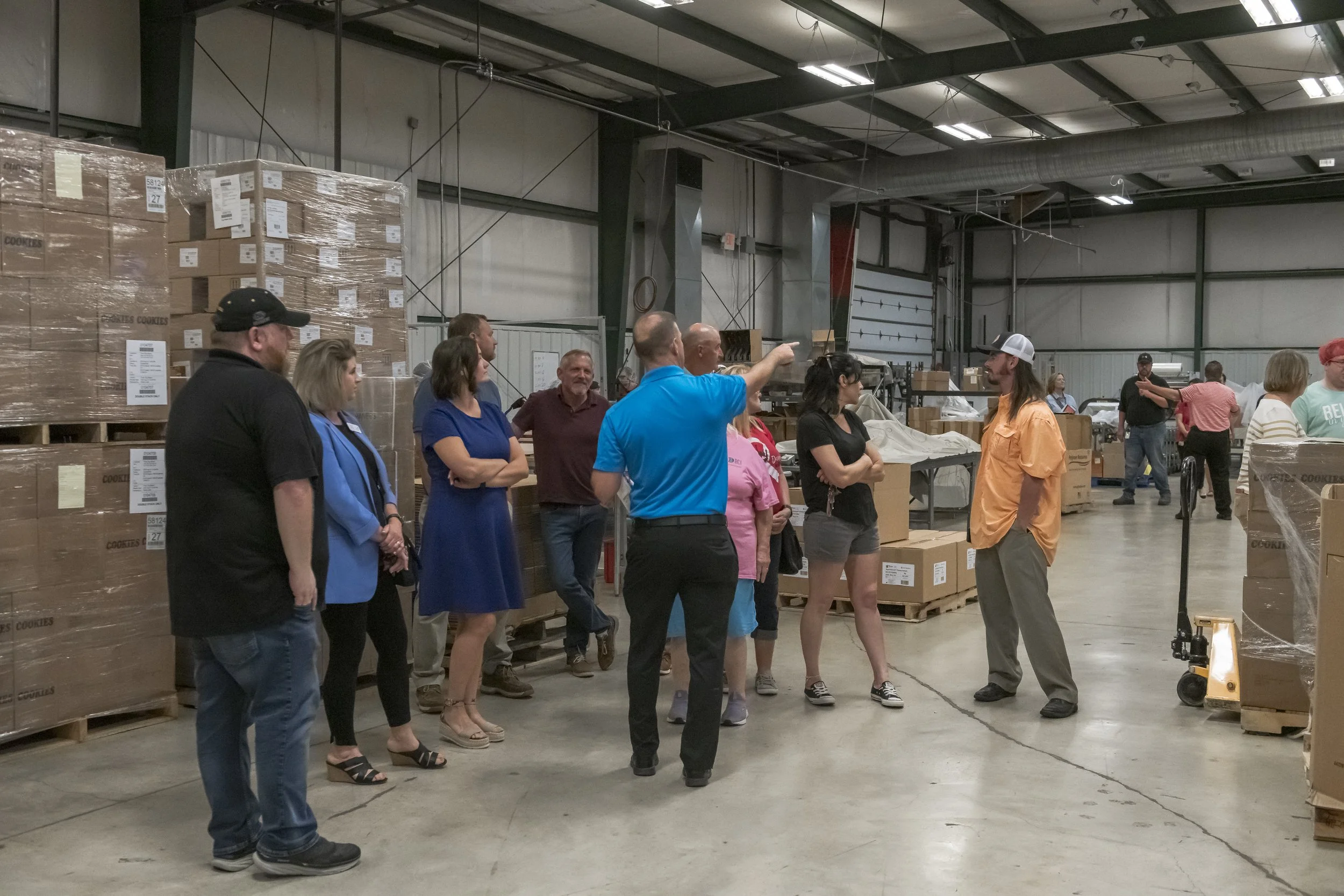 A guide points across the warehouse while visitors watch at the 2022 BCI Open House.