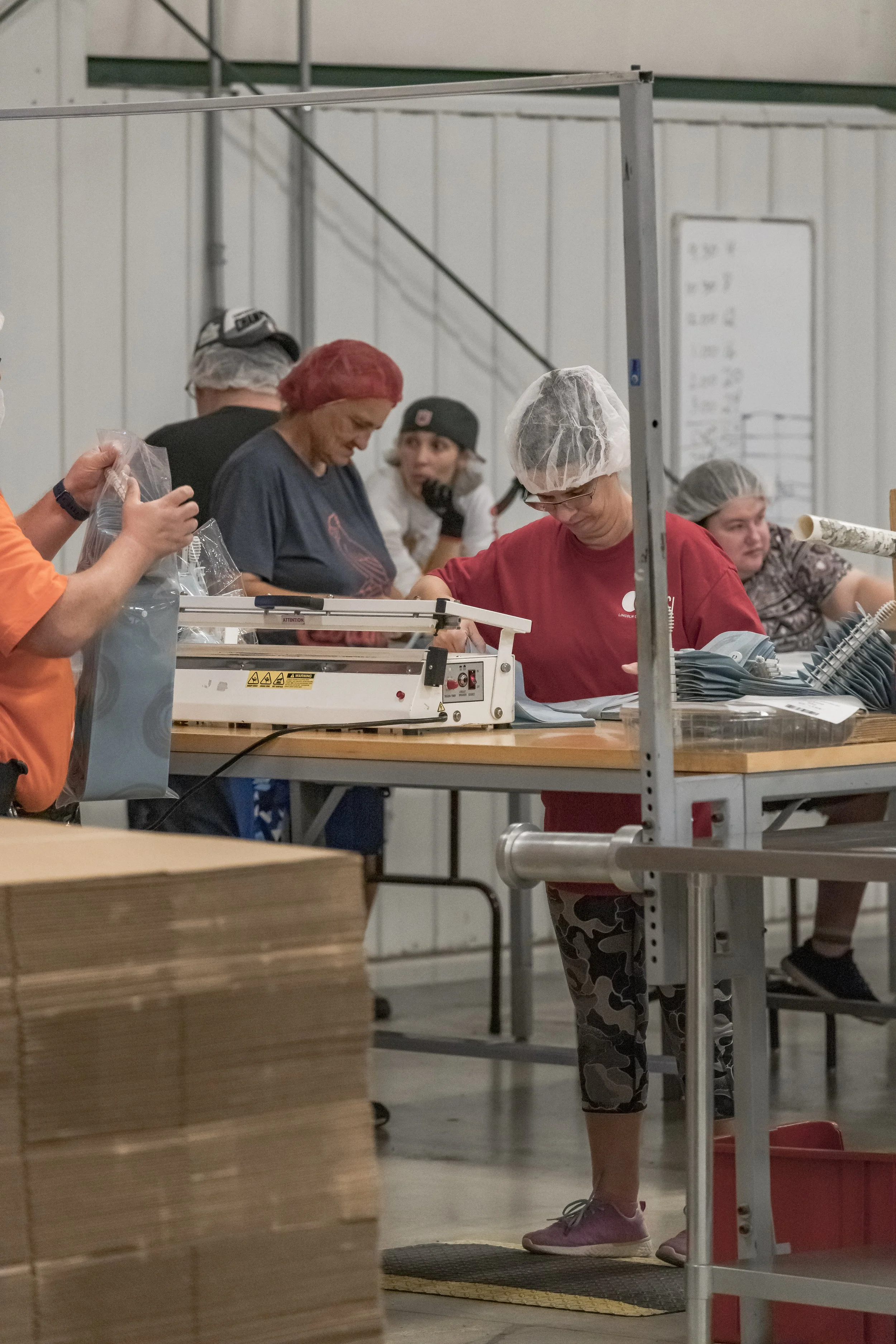 Workers wearing hairnets handle items at a production table at the 2022 BCI Open House.