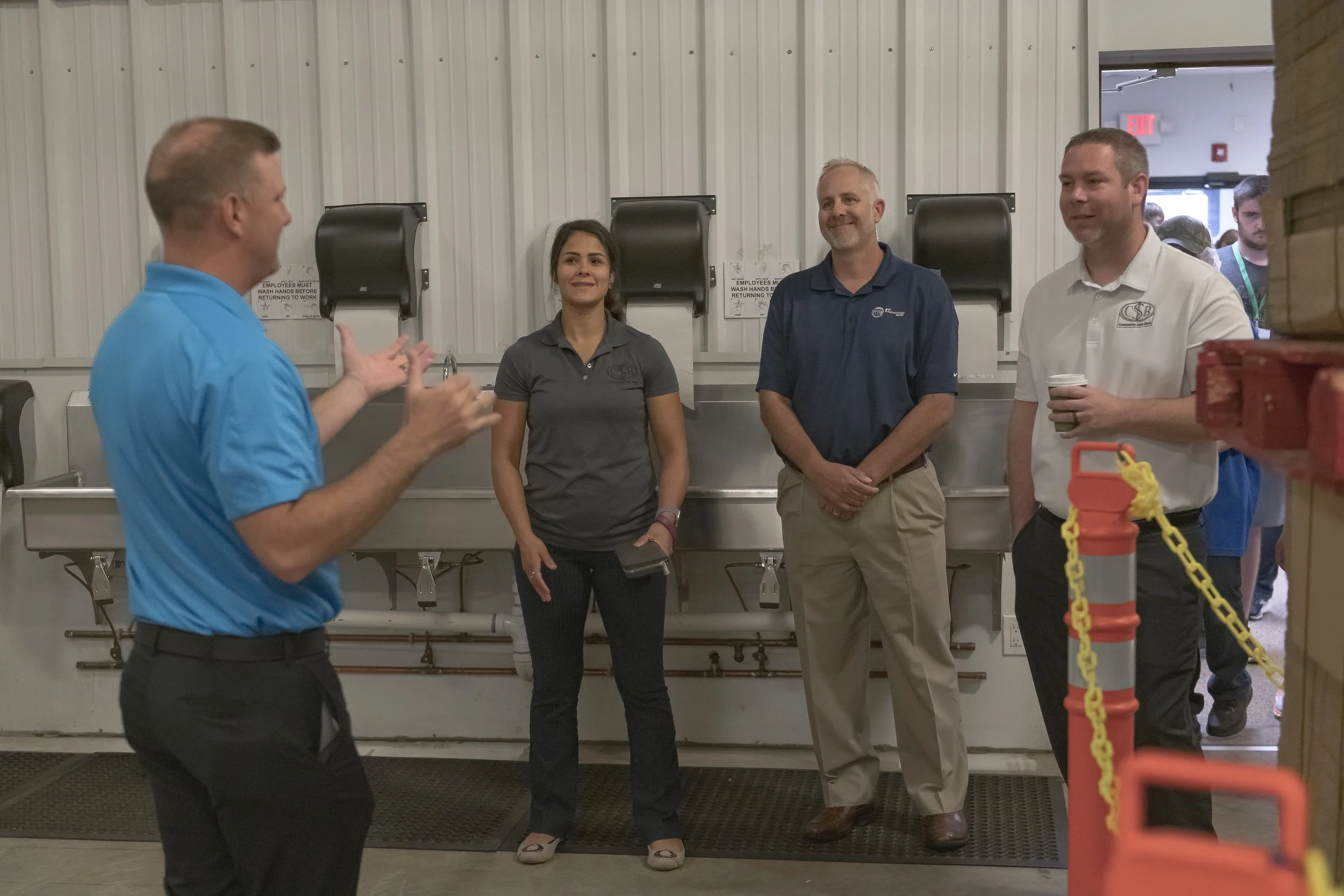 A guide speaks with three visitors beside the facility's sinks at the 2022 BCI Open House.