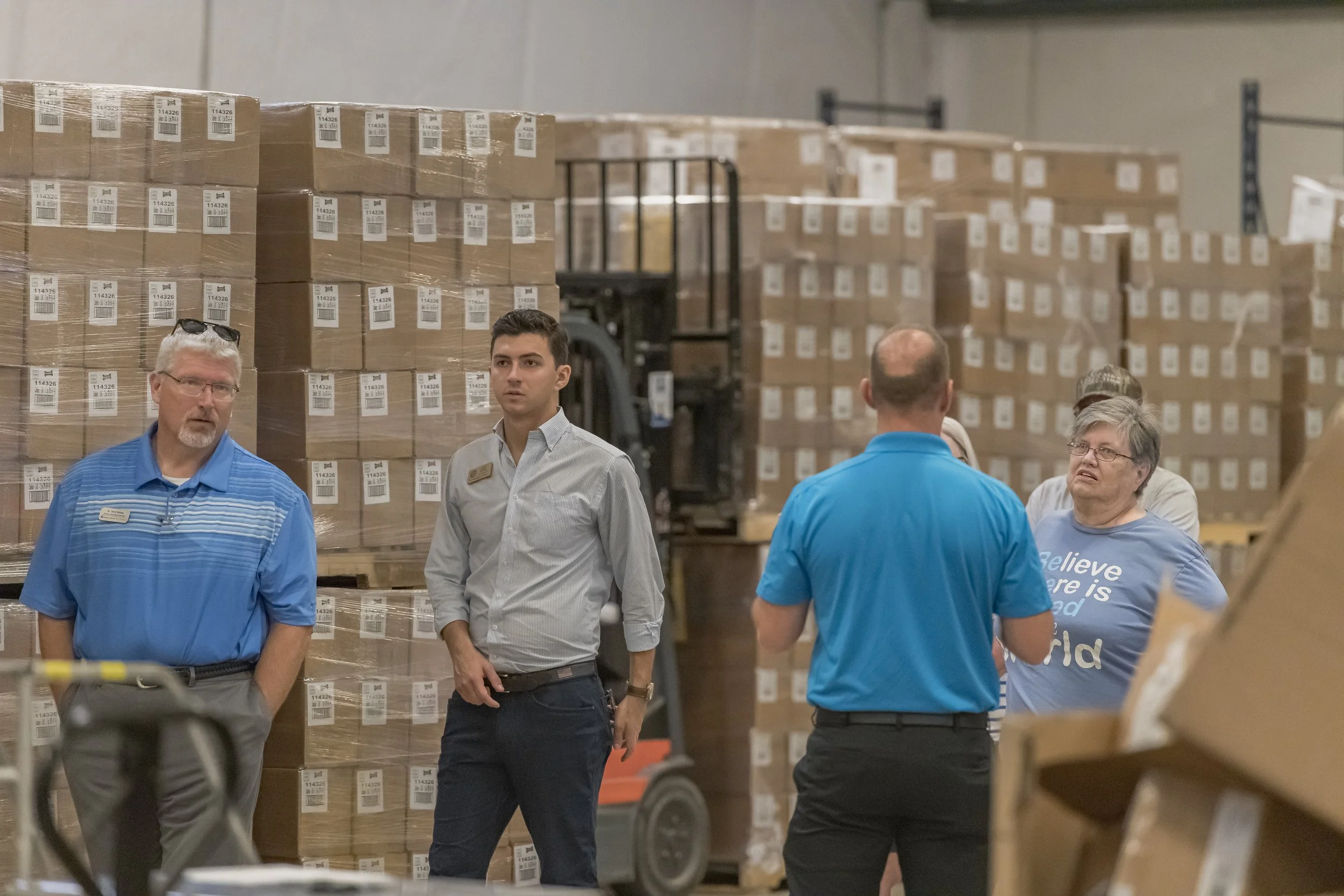 Visitors listen to a guide in front of tall stacks of boxed products at the 2022 BCI Open House.