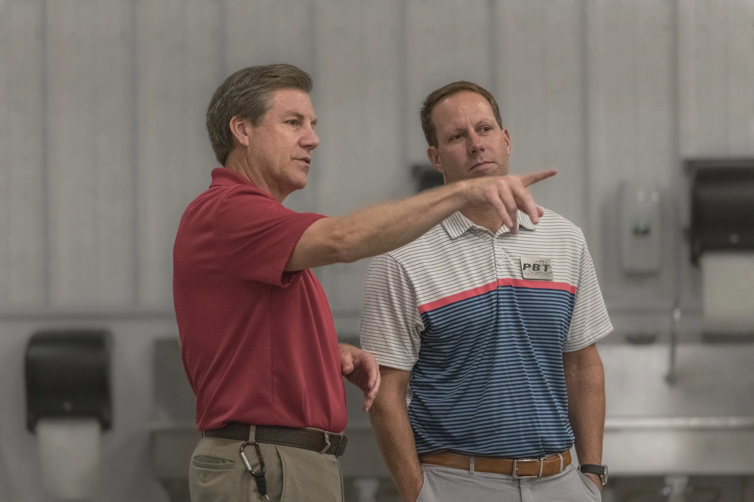 An attendee in a red polo points across the production area while another looks on at the 2022 BCI Open House.