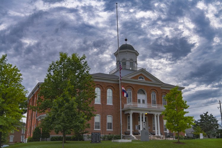 A red-brick courthouse and its cupola rise beneath textured clouds in Troy, Missouri.