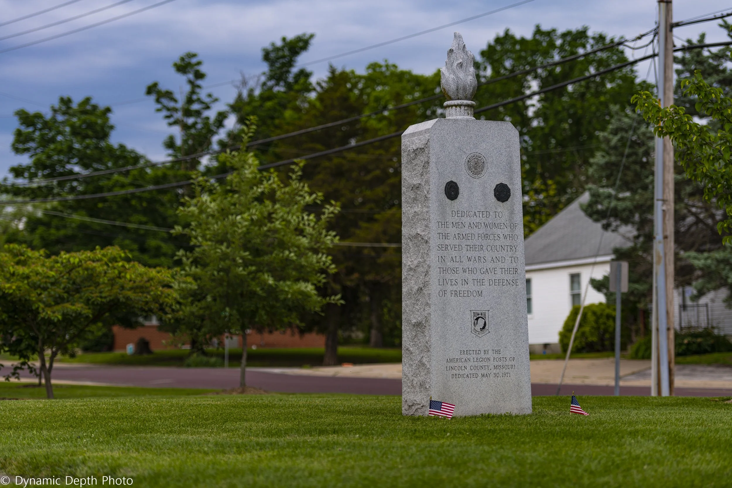 A white stone memorial stands on the lawn with small American flags at its base.