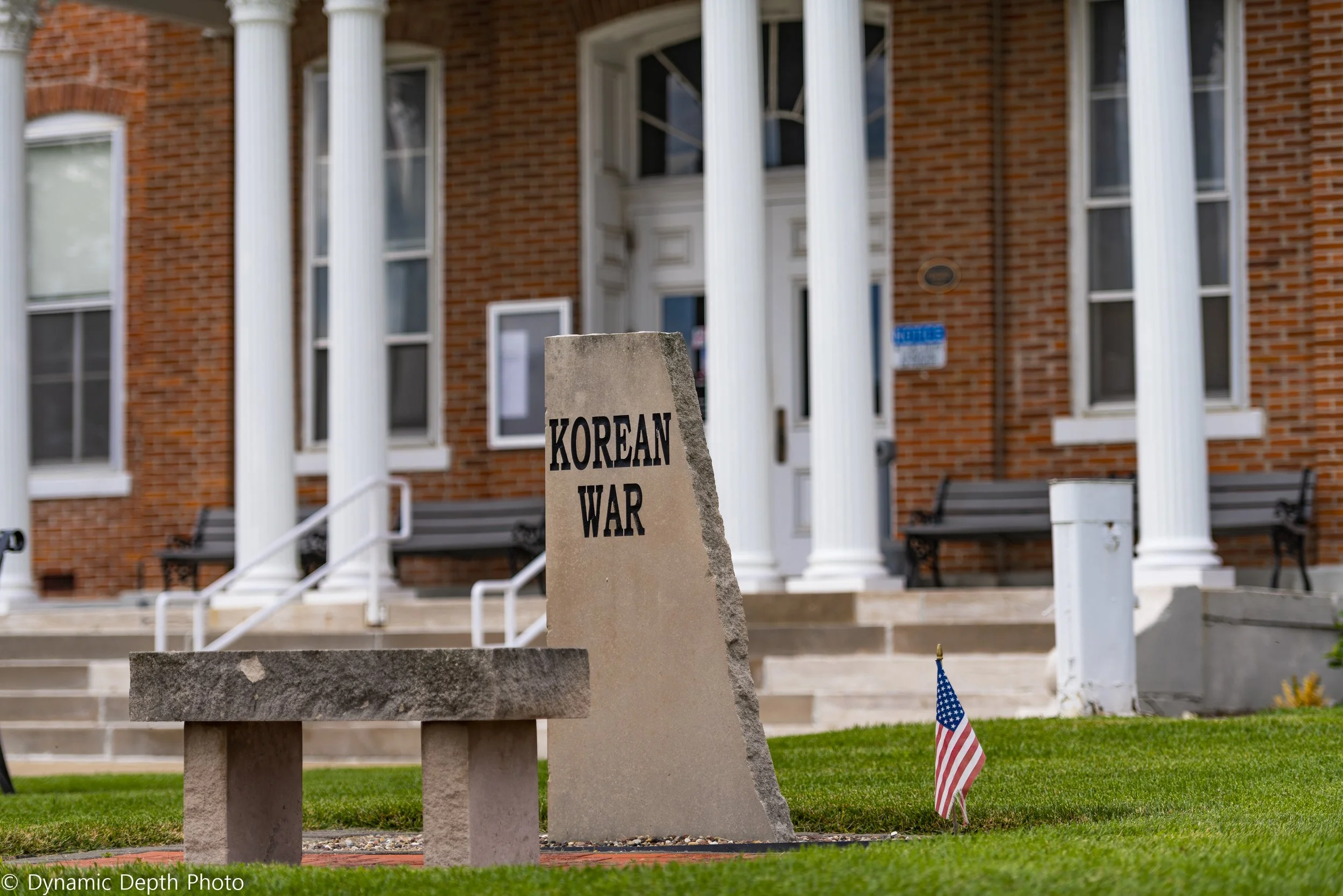 A Korean War memorial and stone bench stand beside the building's white columns.
