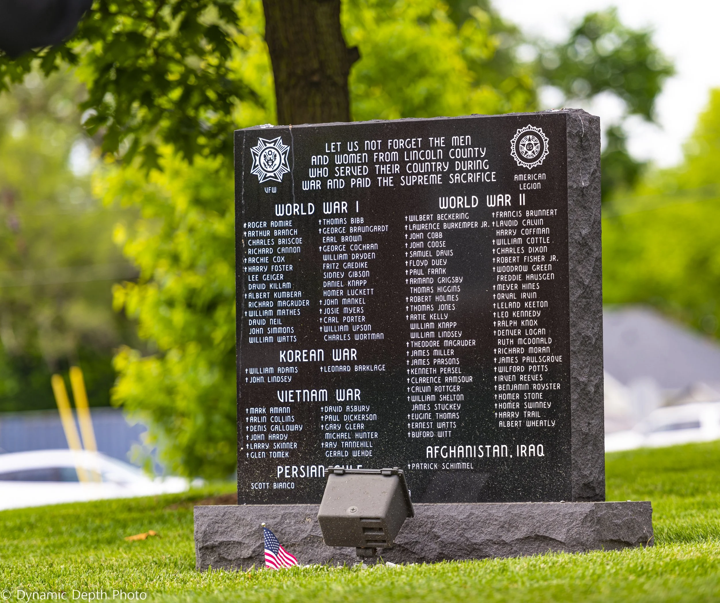 A dark stone memorial lists Lincoln County service members beneath the shade of a tree.