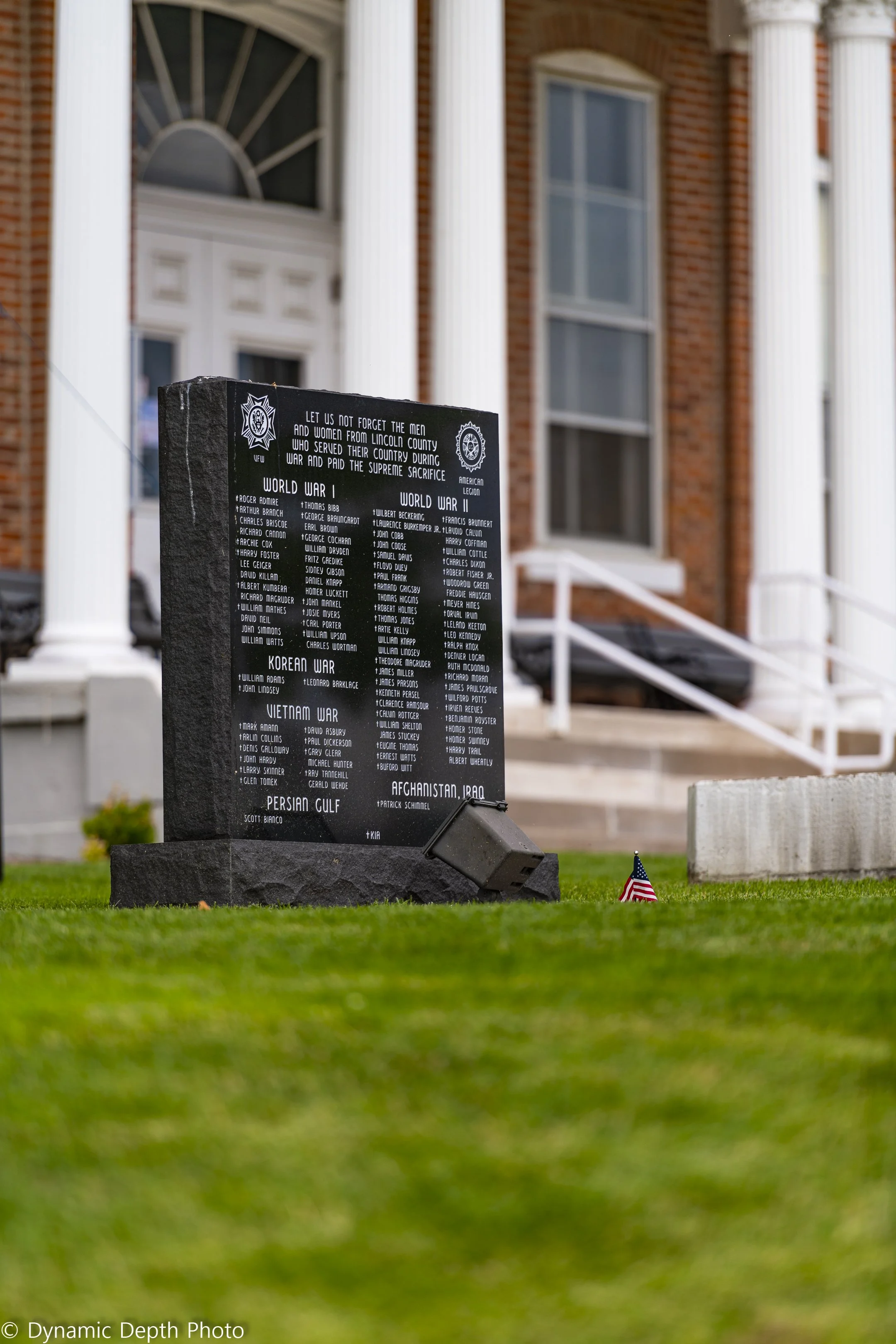 A side view of the dark memorial stone shows the brick building and entrance steps behind it.
