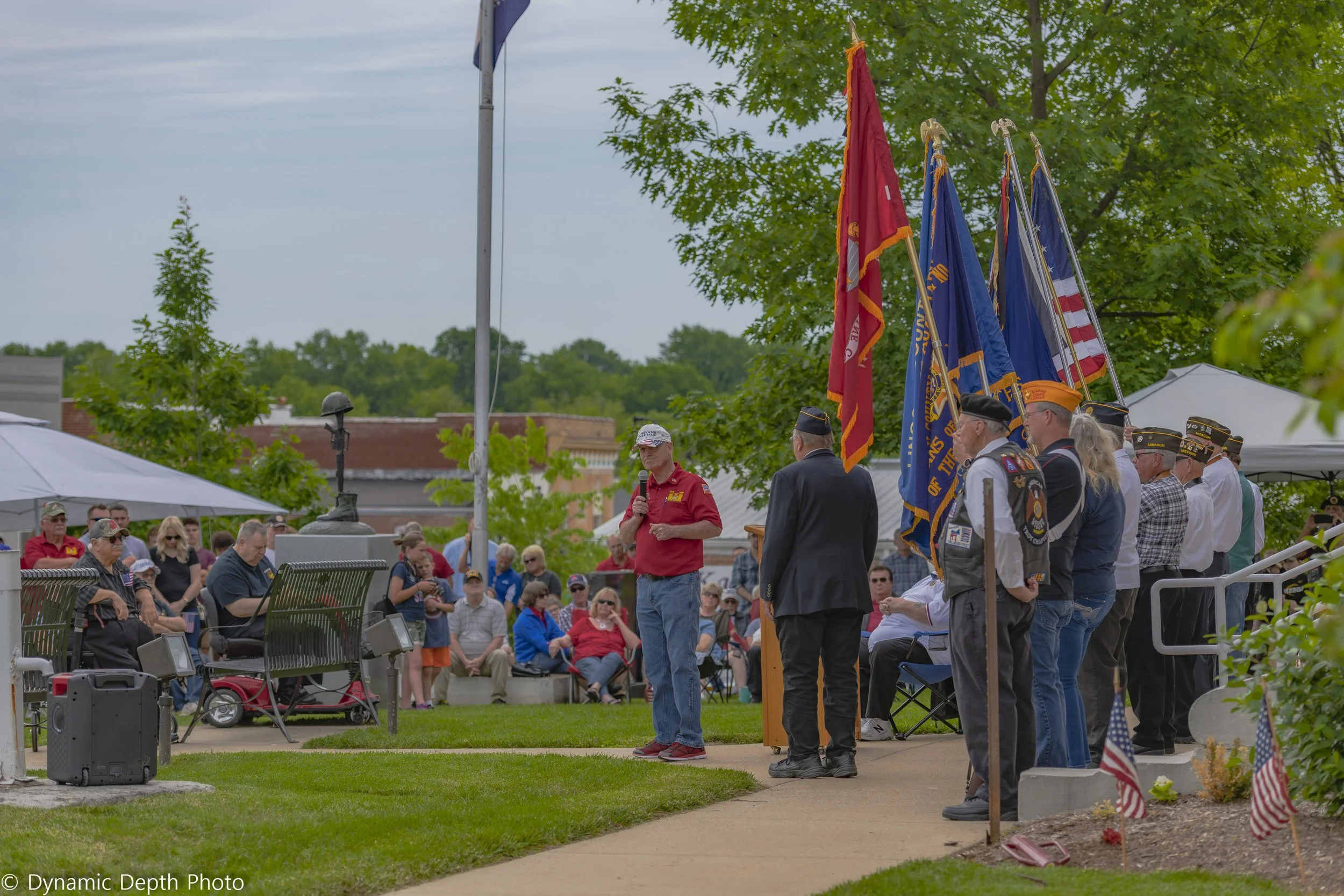 A speaker stands beside flag bearers while attendees sit on the lawn during the 2021 Memorial Day Service.