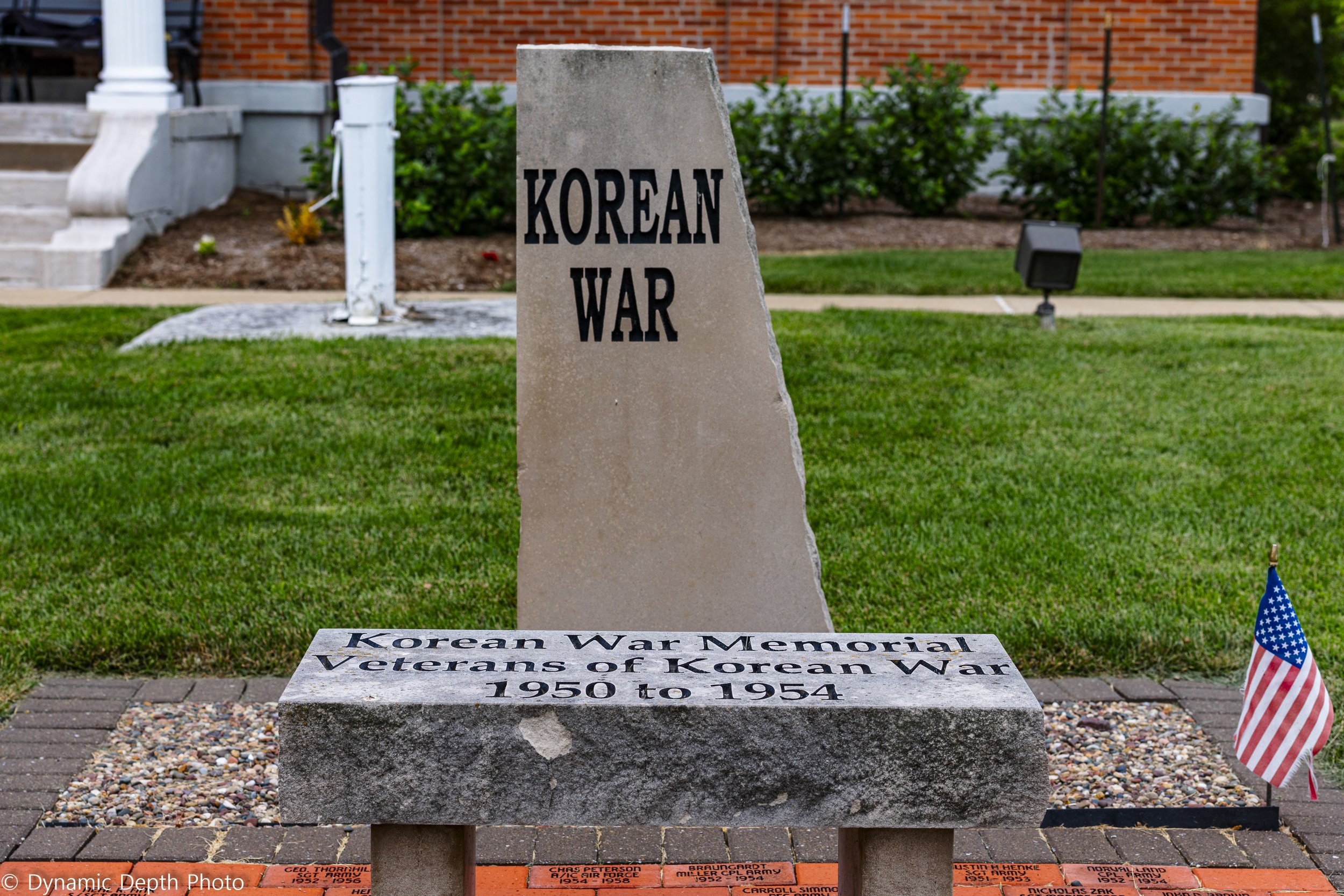 A Korean War memorial and inscribed bench are framed by a small American flag.