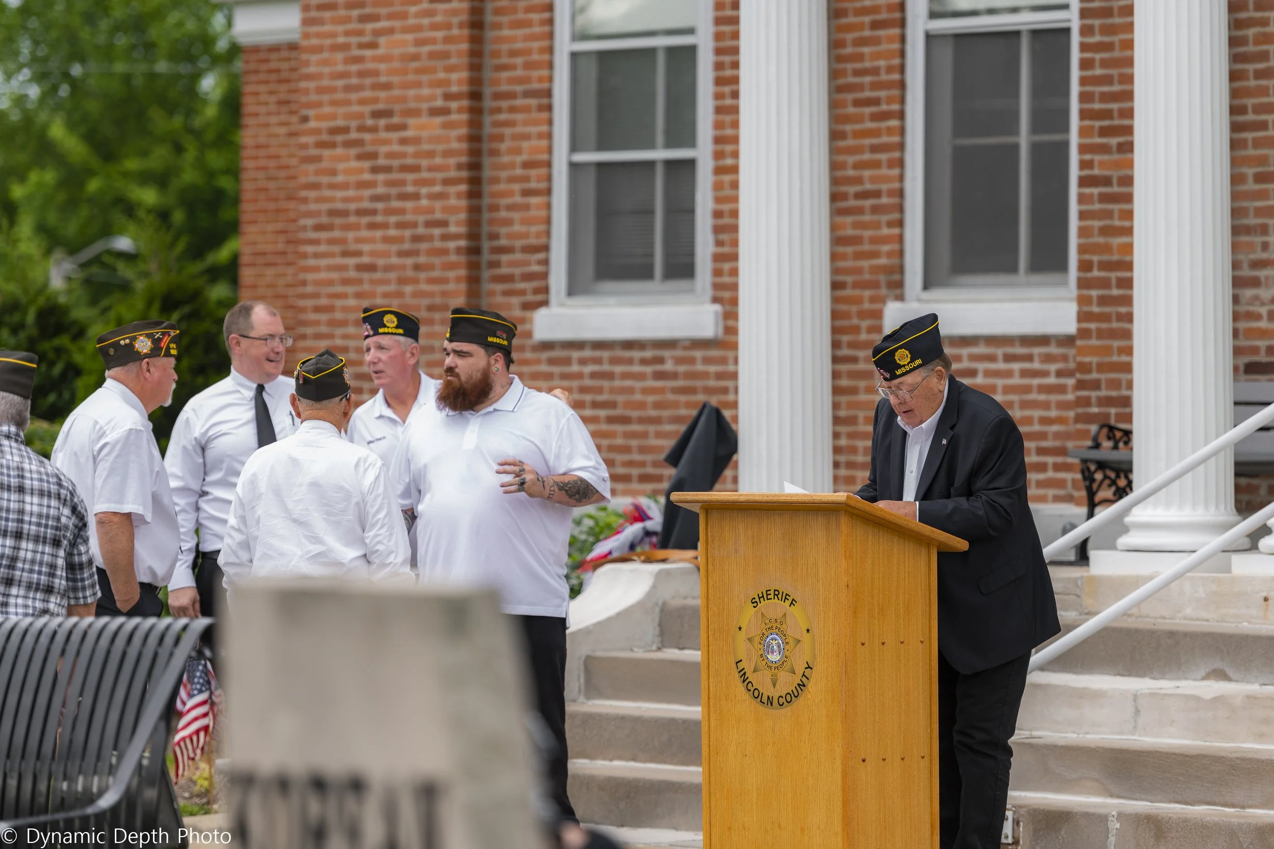 Participants gather beside a speaker reading at the lectern during the 2021 Memorial Day Service.