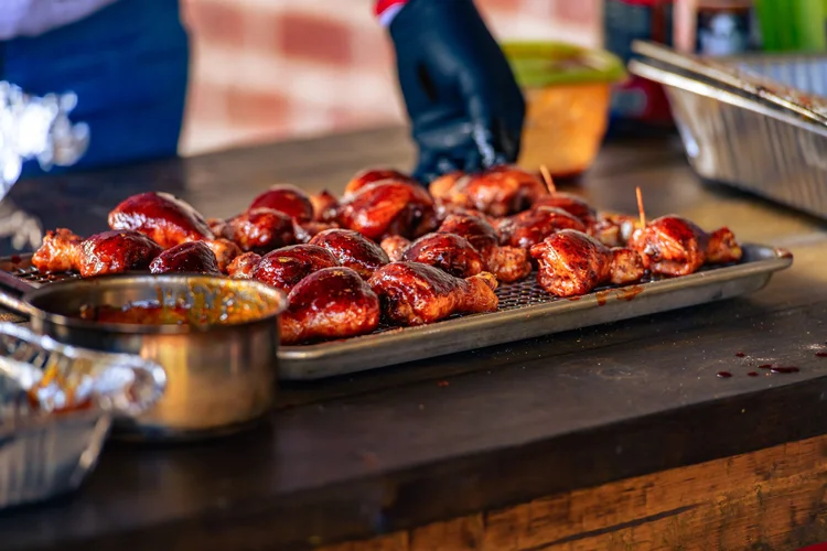 Glazed chicken rests on a metal tray beside a bowl of sauce.