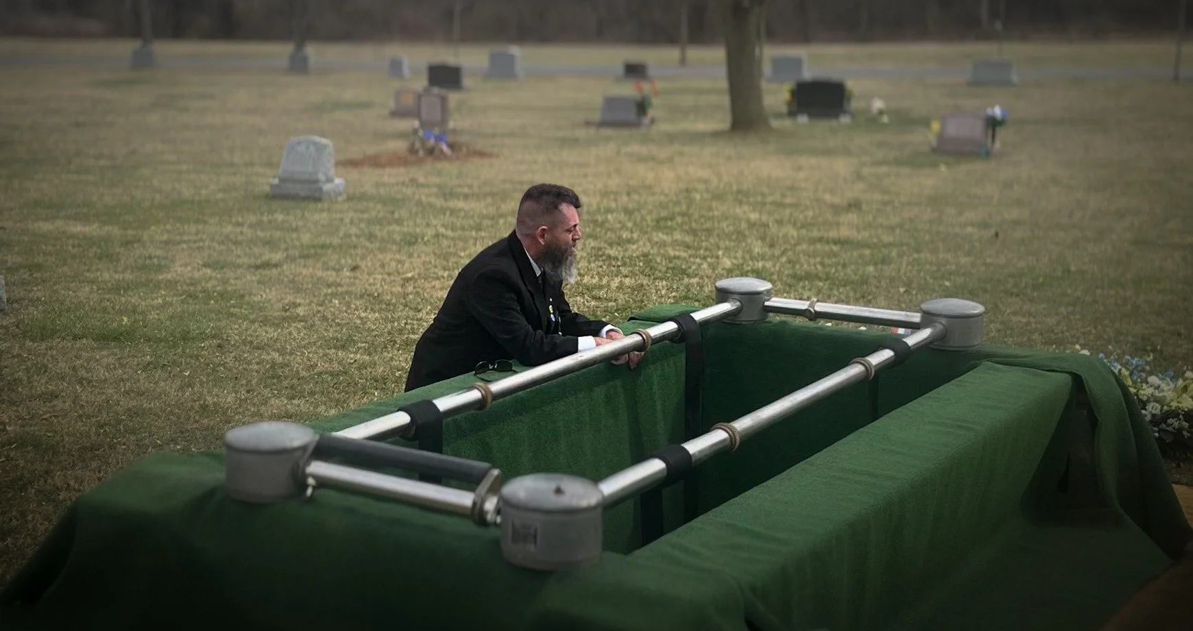 A man kneeling beside the grave during a quiet moment at the cemetery