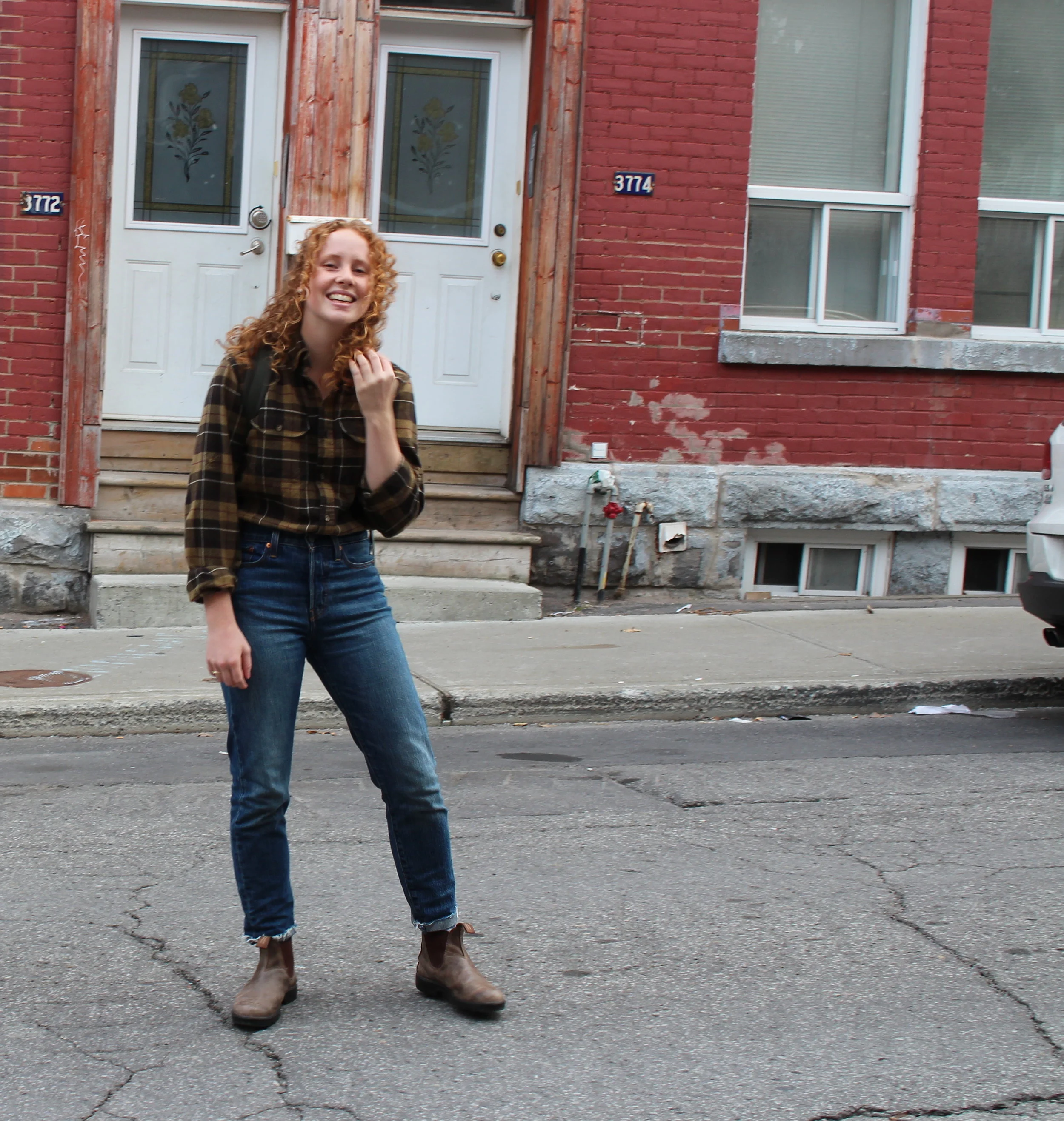 girl posing in front of house with jeans, flannel, and backpack
