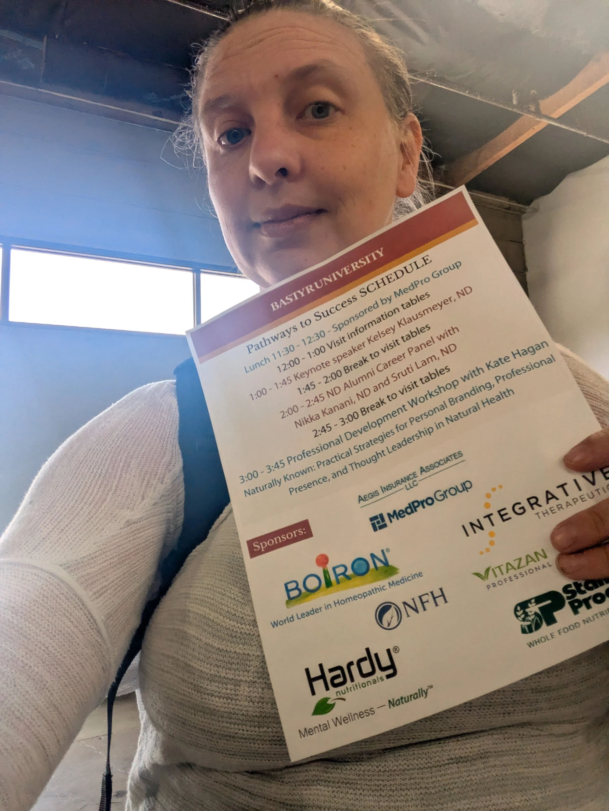 A person holding a brochure or program at a conference or event, with text outlining the schedule and sponsors of the event, including various organizations and logos.