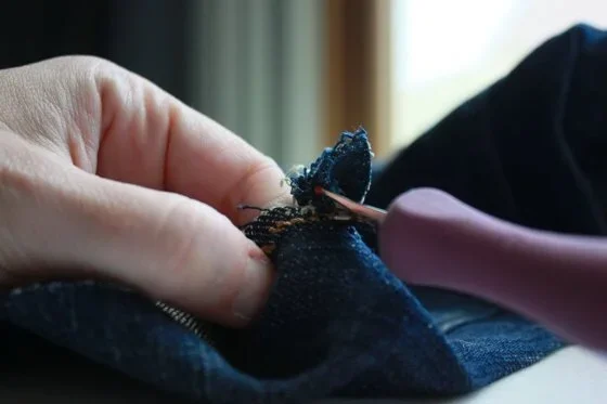The seam ripper being used to open the seam in a pair of jeans
