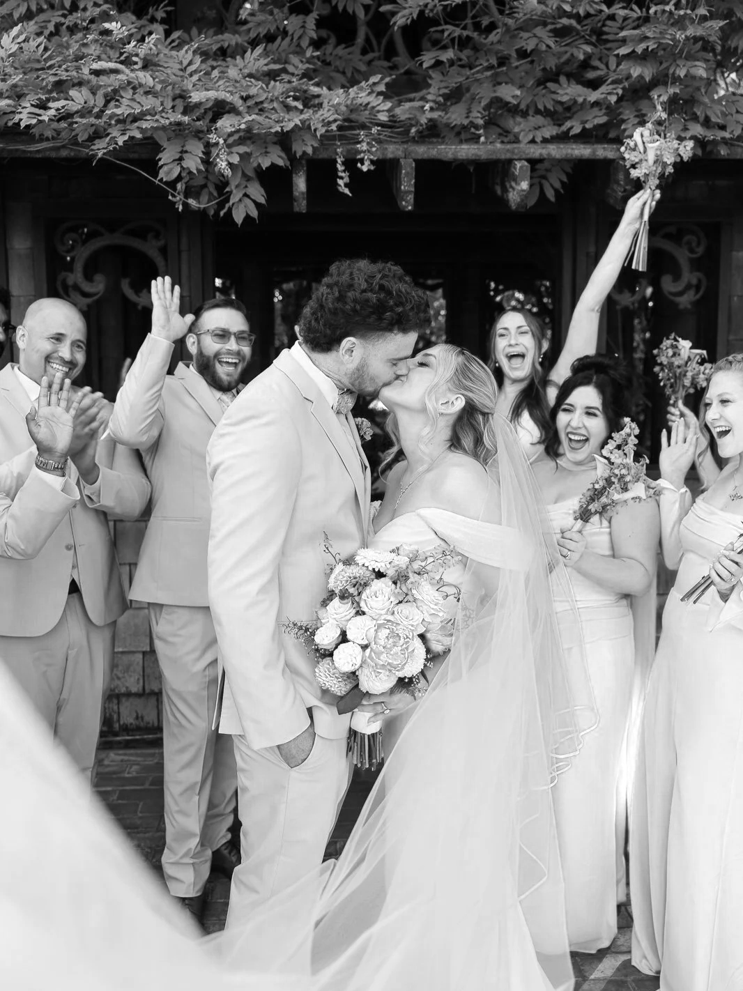Bride and groom share a kiss and wedding party celebrates