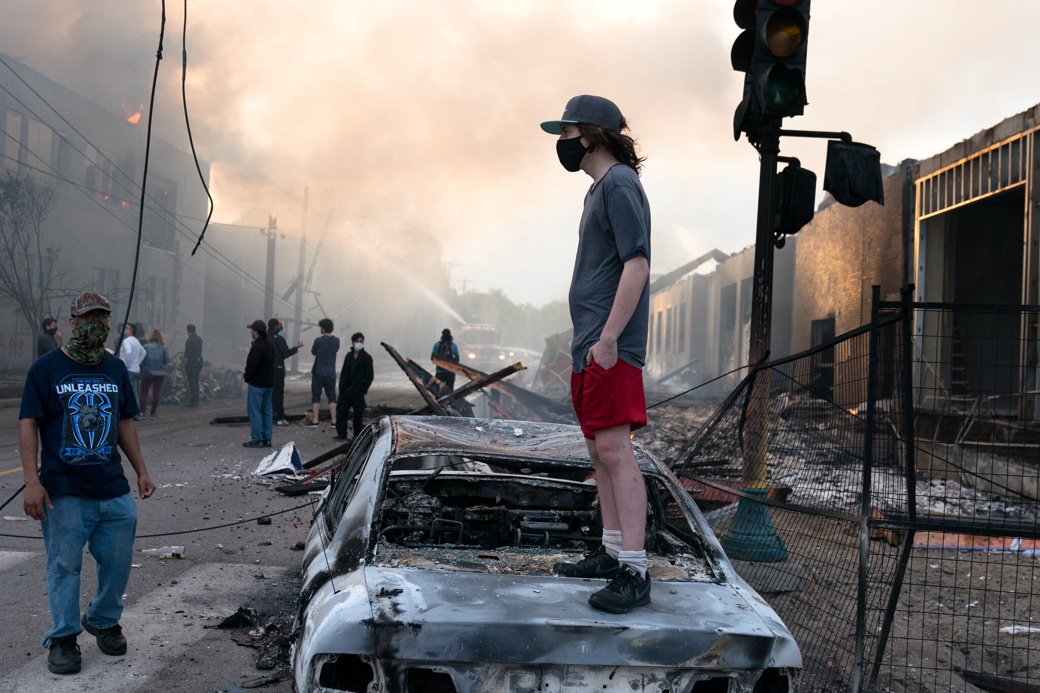  A man stands on a burned car on Thursday morning as fires burn behind him in the Lake St area of Minneapolis, Minnesota 