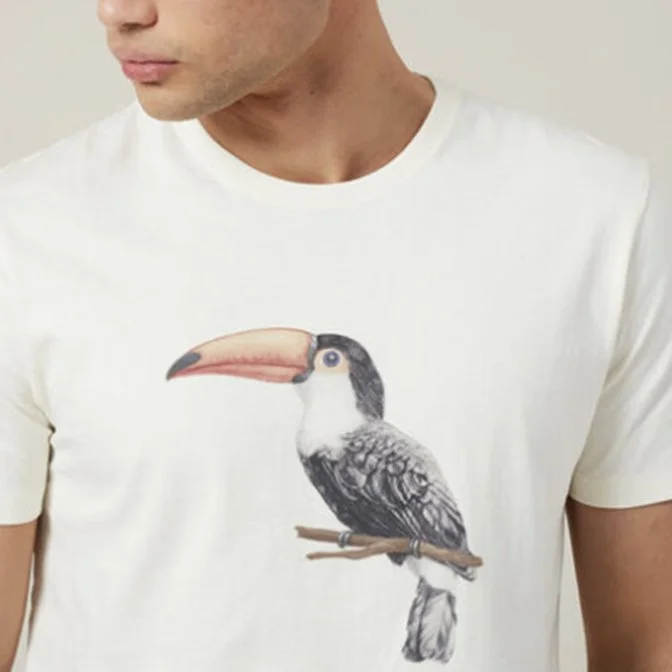 A person wearing a white T-shirt featuring a realistic illustration of a toucan bird with a large orange beak.