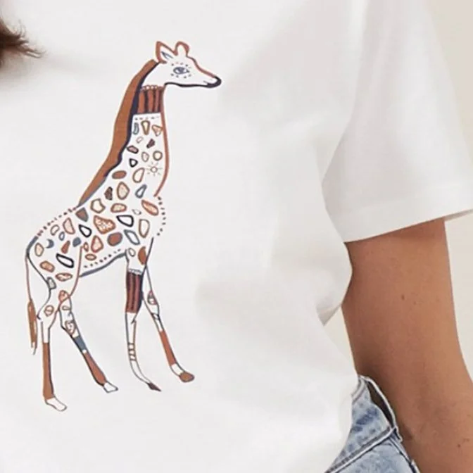 Close-up of a white t-shirt featuring a whimsical illustration of a giraffe with colorful patches and patterns.