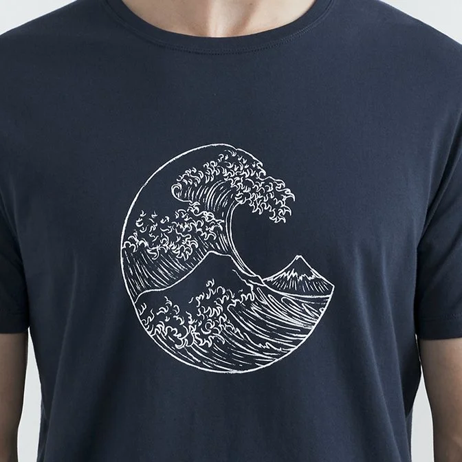 A person wearing a navy blue t-shirt with a white line drawing of a large ocean wave and a mountain inside a circle.