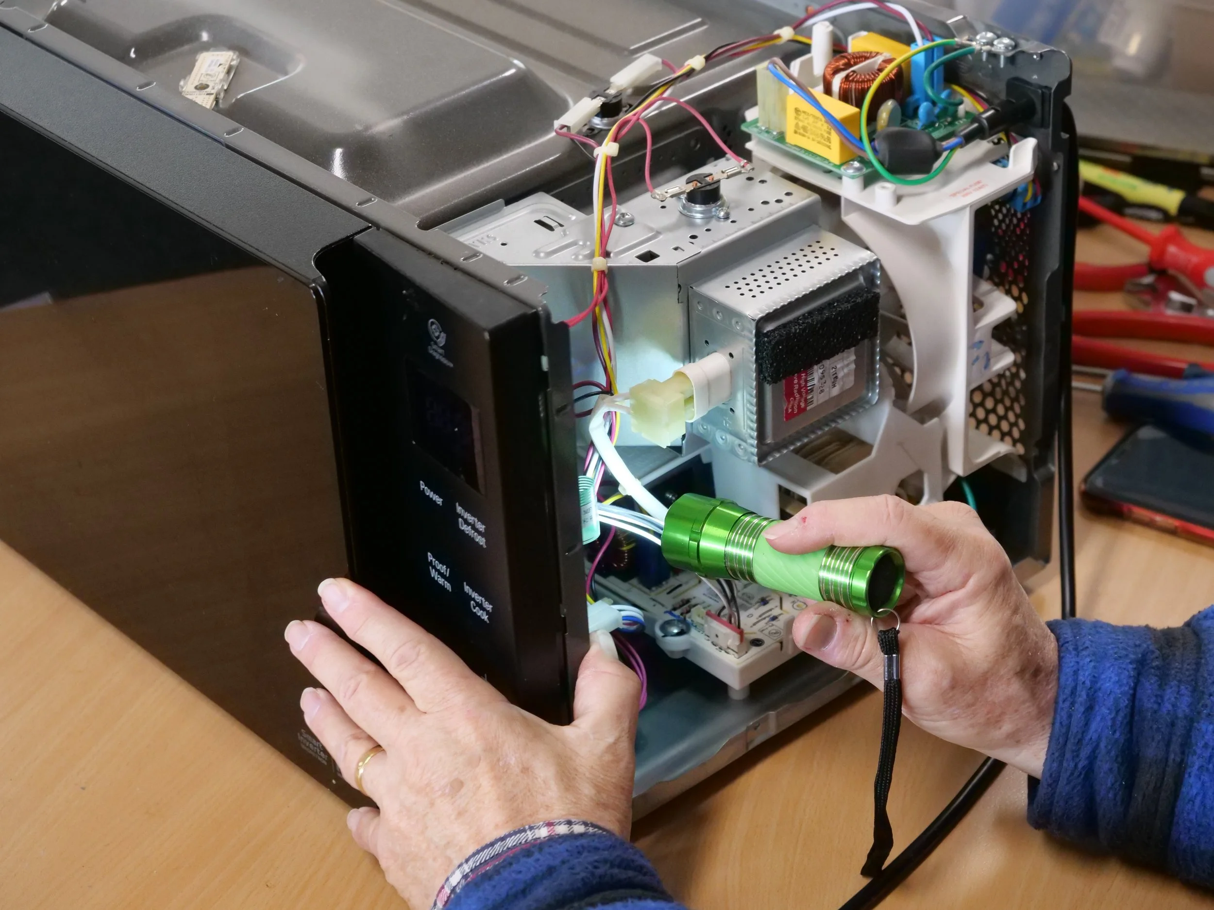 Hands holding torch inside circuitry of microwave.