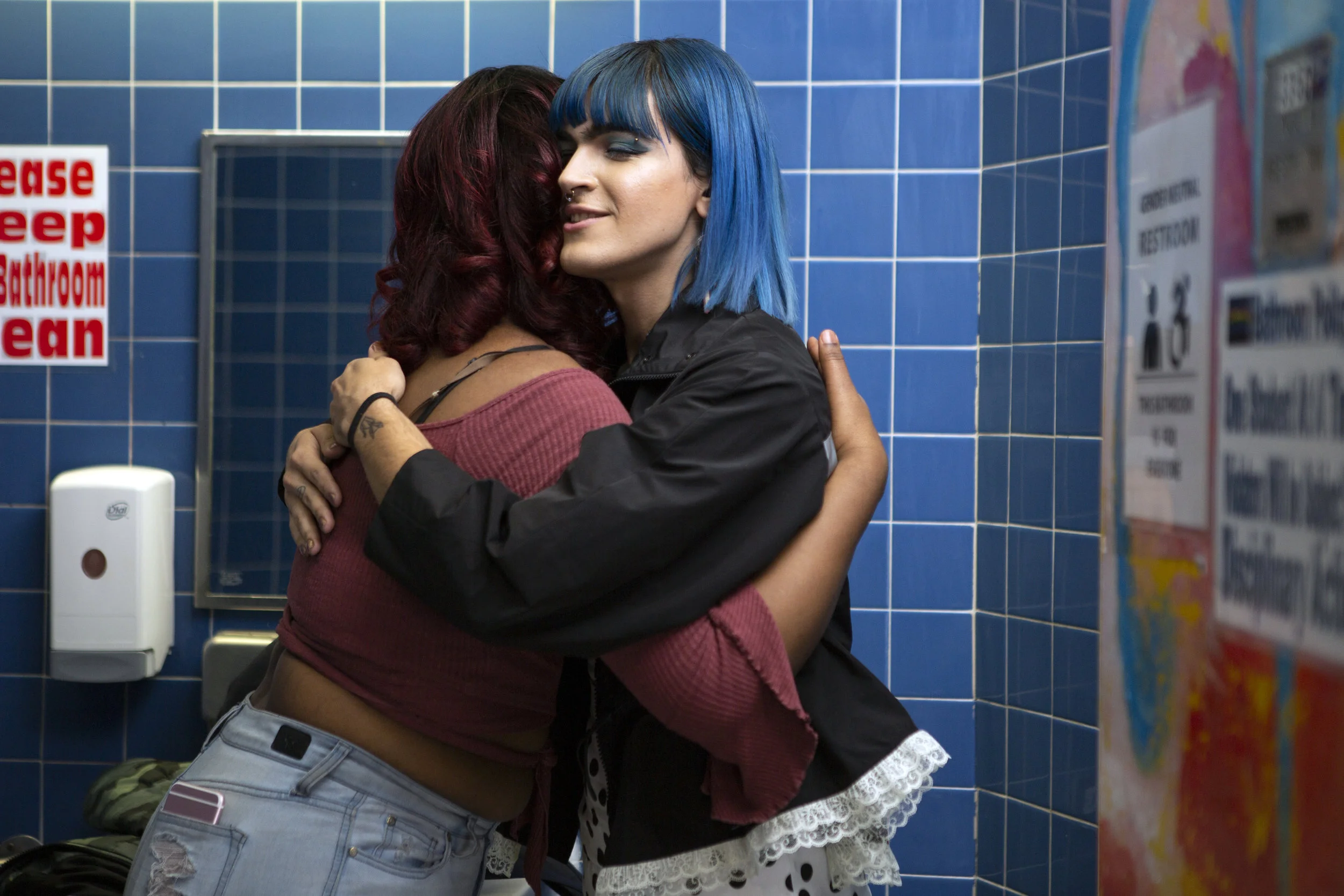 A non-binary femme embracing another student in a scbool bathroom.jpg