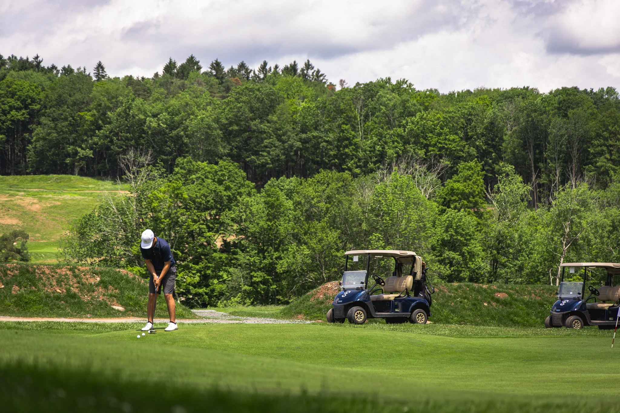 A person preparing to hit a golf ball on a golf course with trees and golf carts in the background.