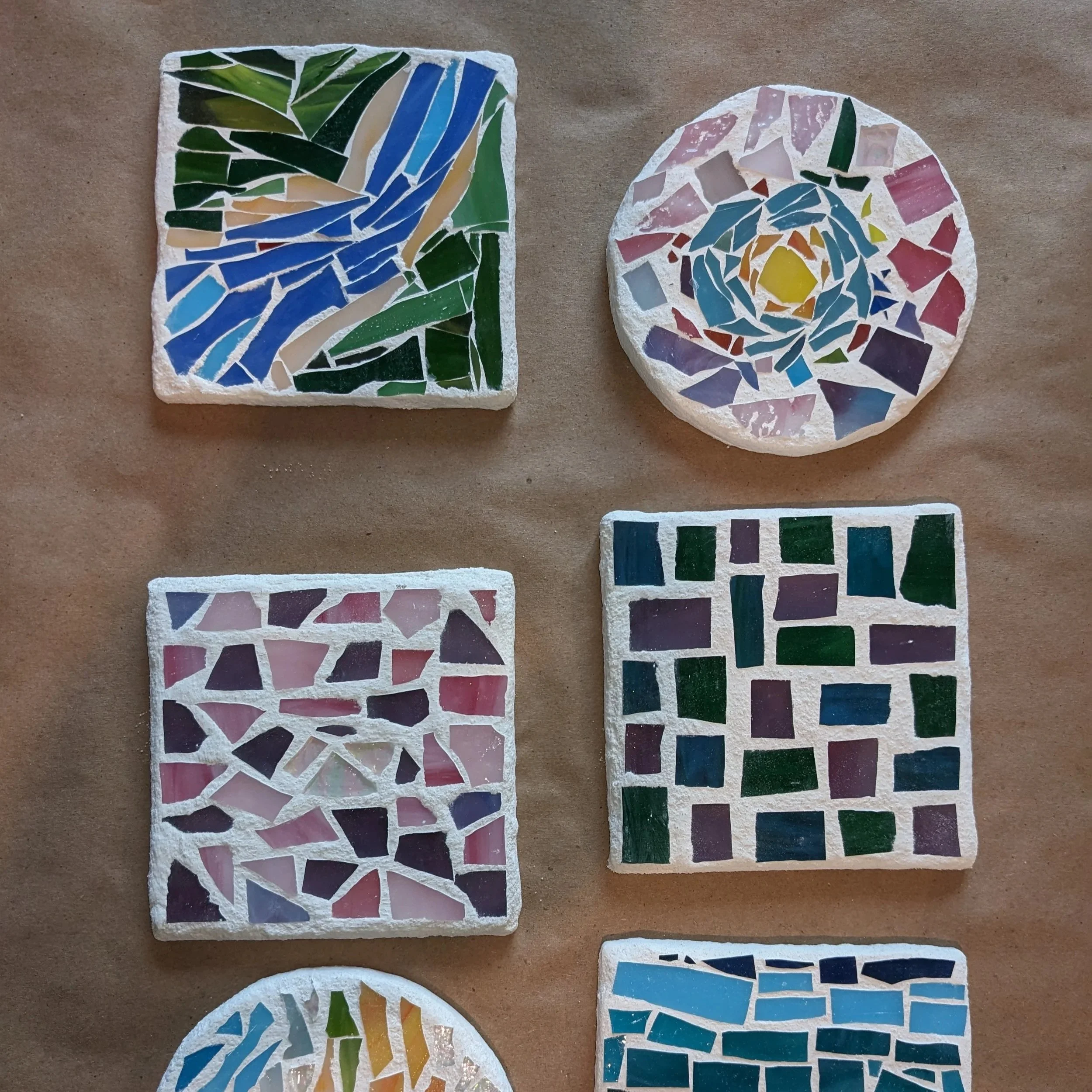 Six colorful mosaic tiles on a brown surface, each with different abstract patterns and shapes.