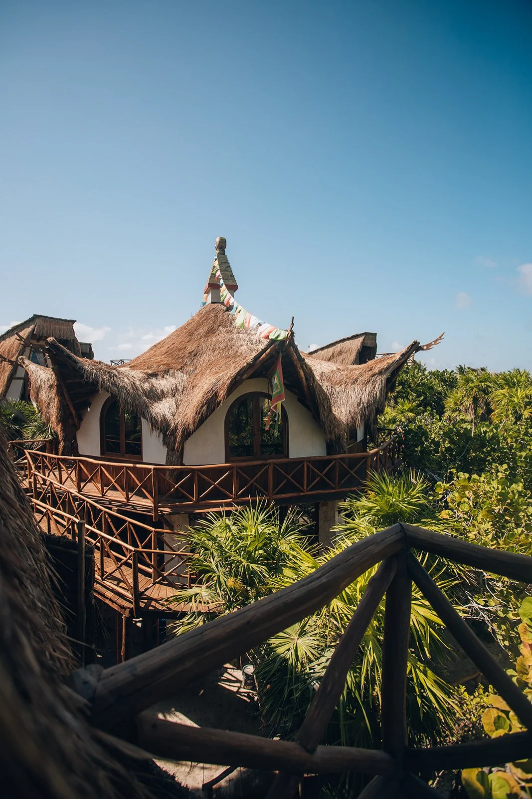 Treehouse with a thatched roof, surrounded by lush tropical foliage, under a clear blue sky.