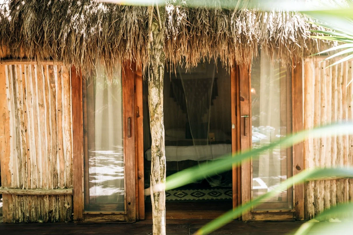Front view of a hut with sliding wooden and glass doors, partially obscured by green foliage.
