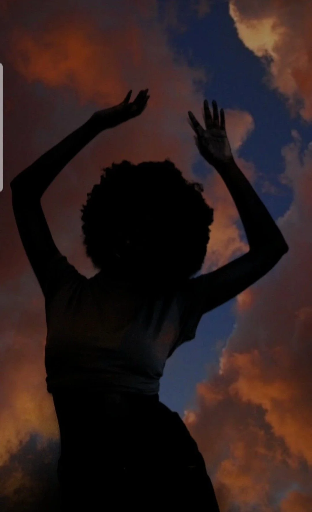 Tulum Reiki Certification Retreat experience. Silhouette of a person with curly hair, raising hands in front of a colorful sky with clouds at sunset or sunrise.