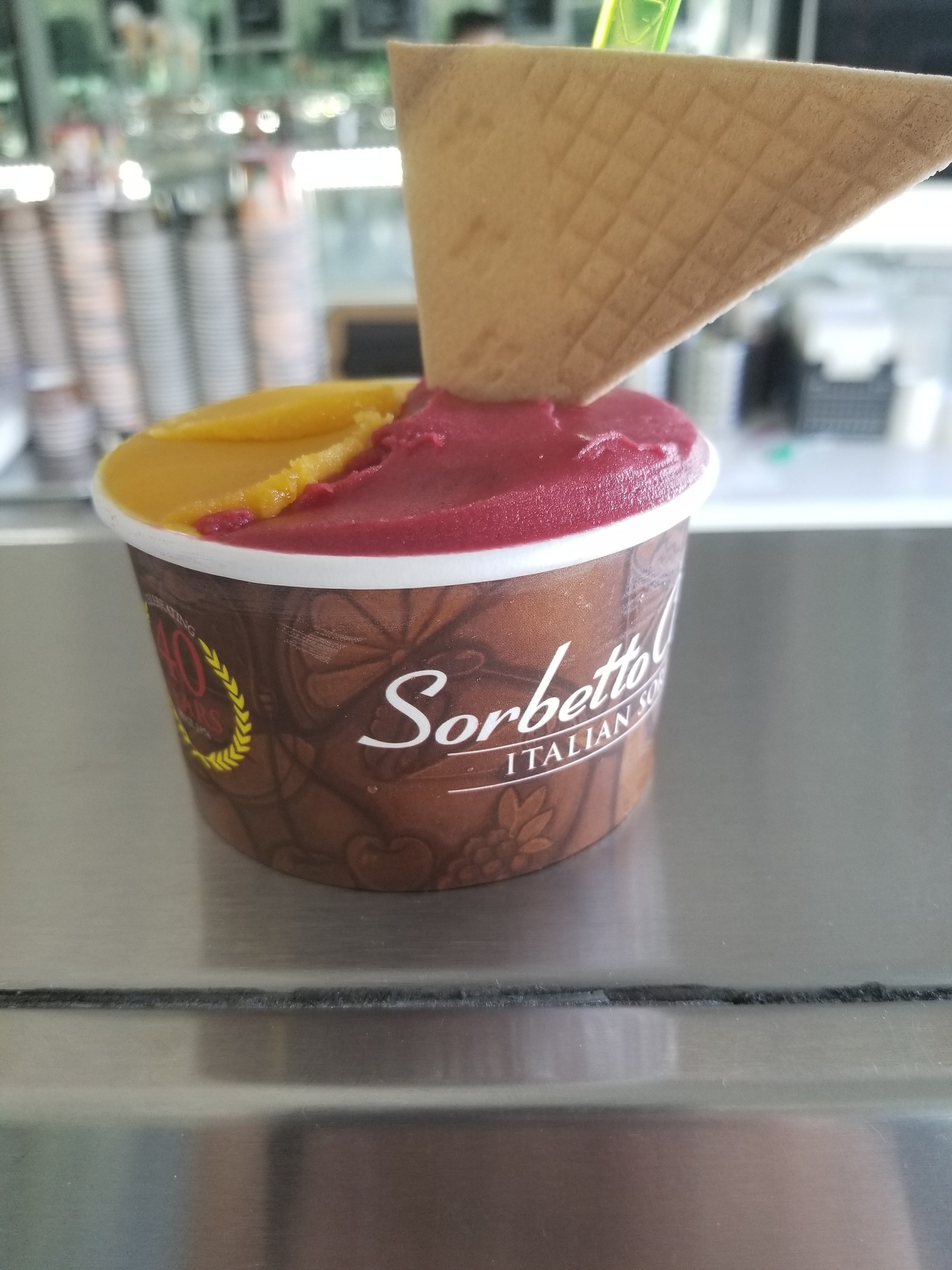 A cup of raspberry and mango sorbet, topped with a triangular wafer cookie.