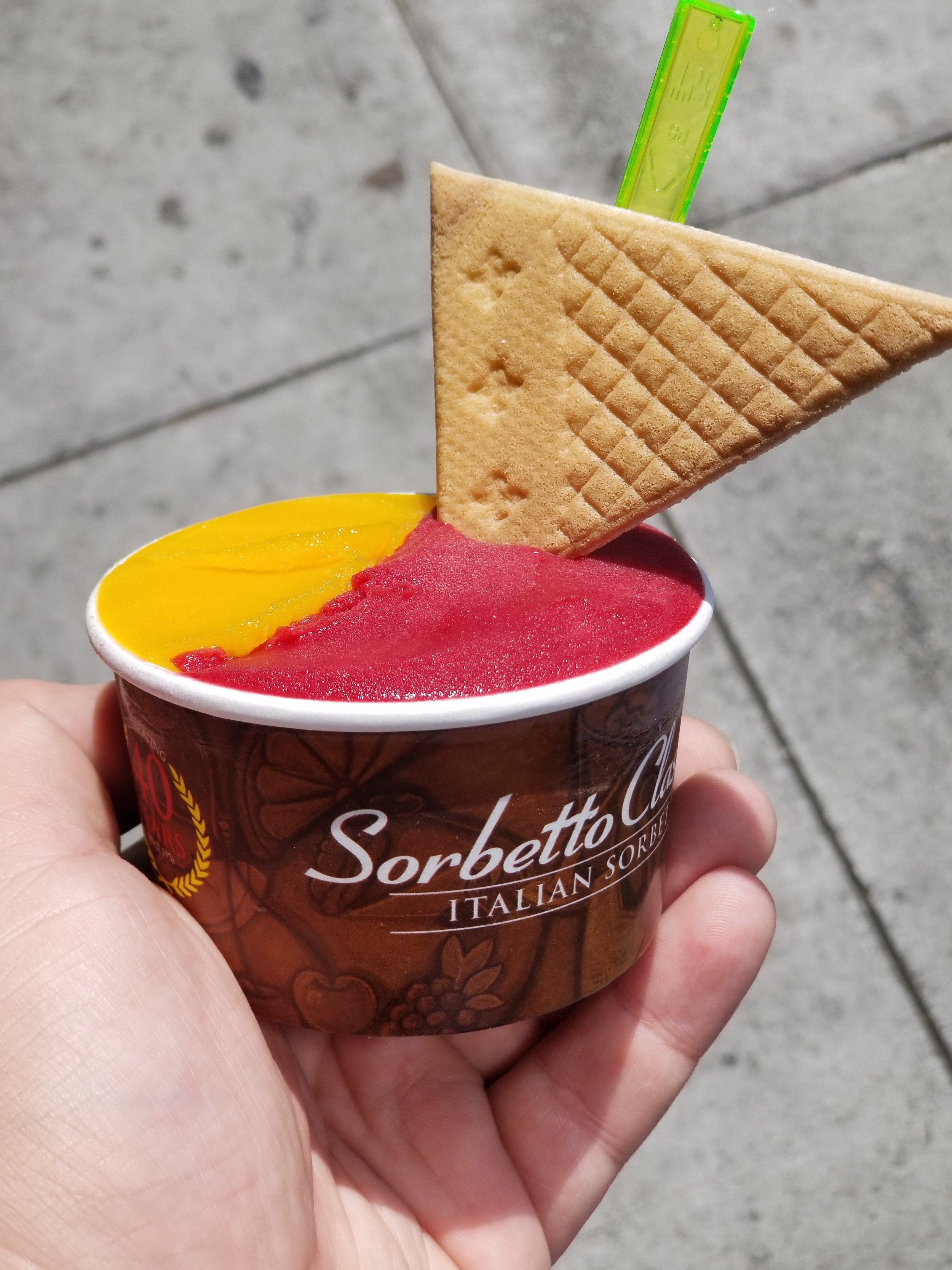 A cup of raspberry and mango sorbets with a triangle wafer cookie.