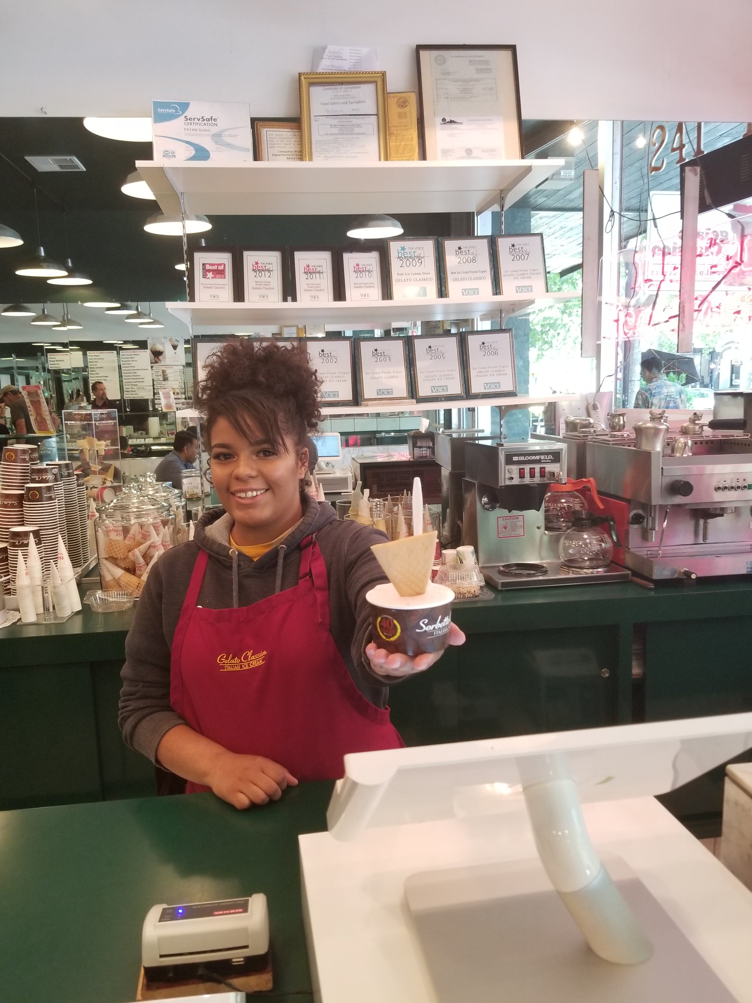 A Gelato Classico employee handing a customer a delicious treat.