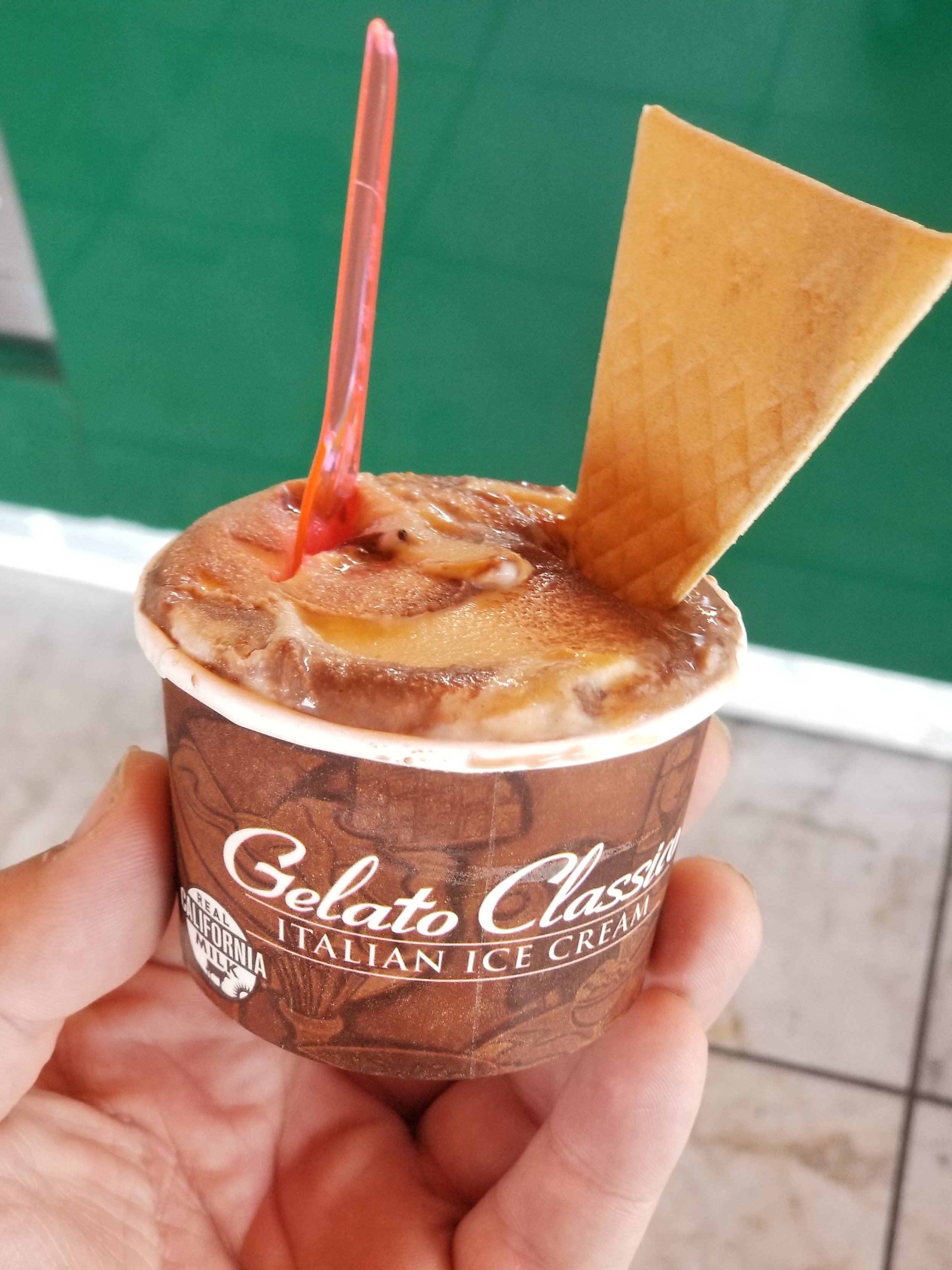 A cup of gelato with an orange spoon and triangular wafer cookie.