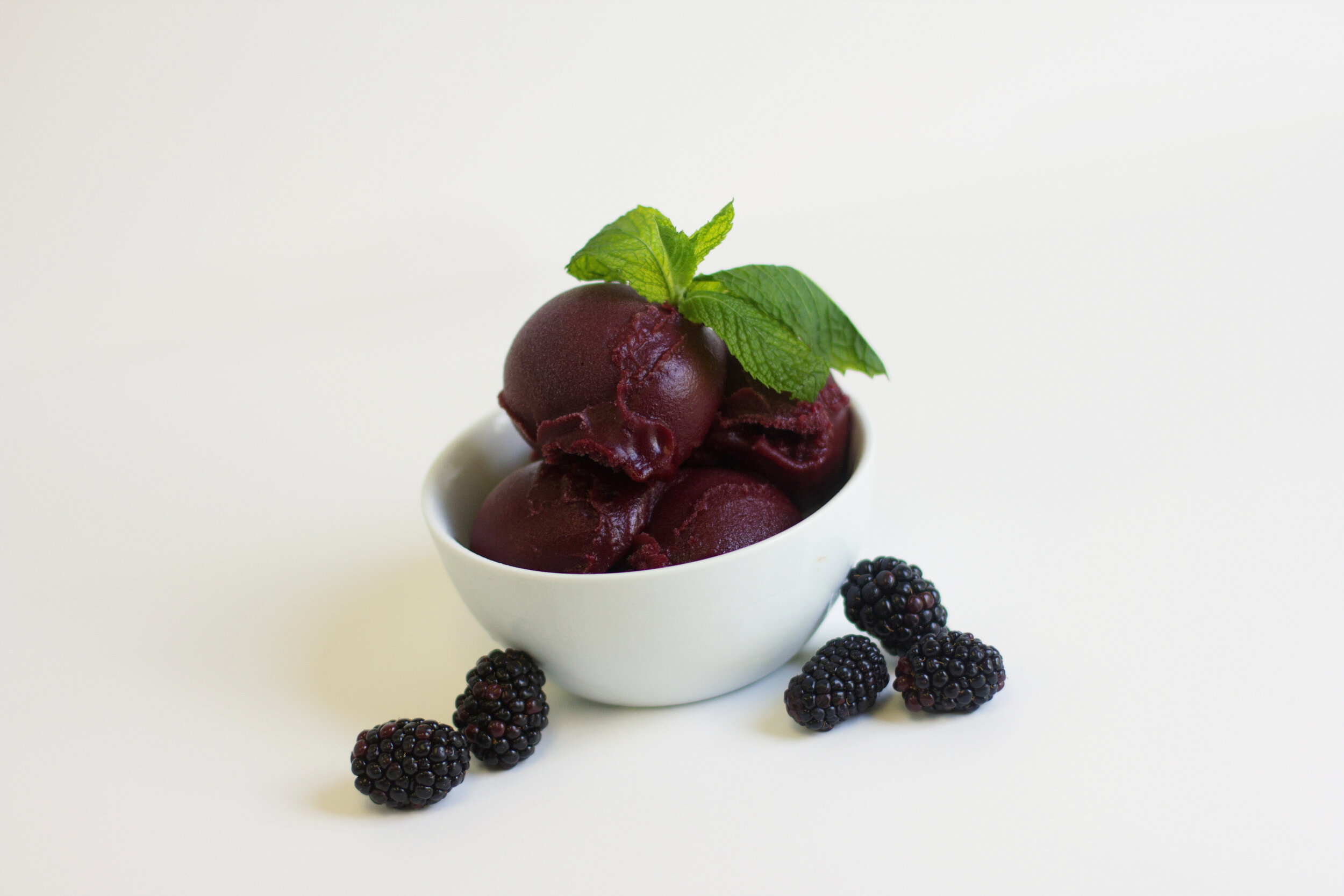 A bowl of blackberry sorbet next to fresh blackberries