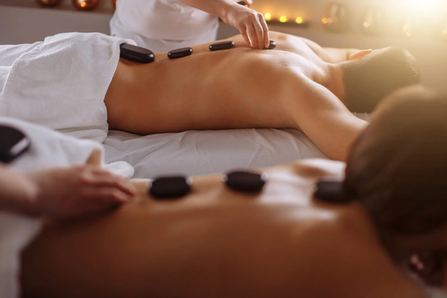 People receiving hot stone massages in a spa treatment room with warm lighting
