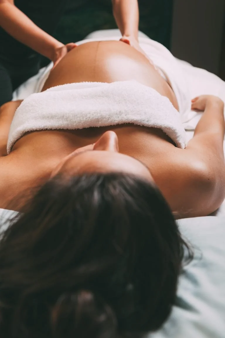 A person lying face up on a massage table receiving a massage, with their back exposed and a towel across their lower back.