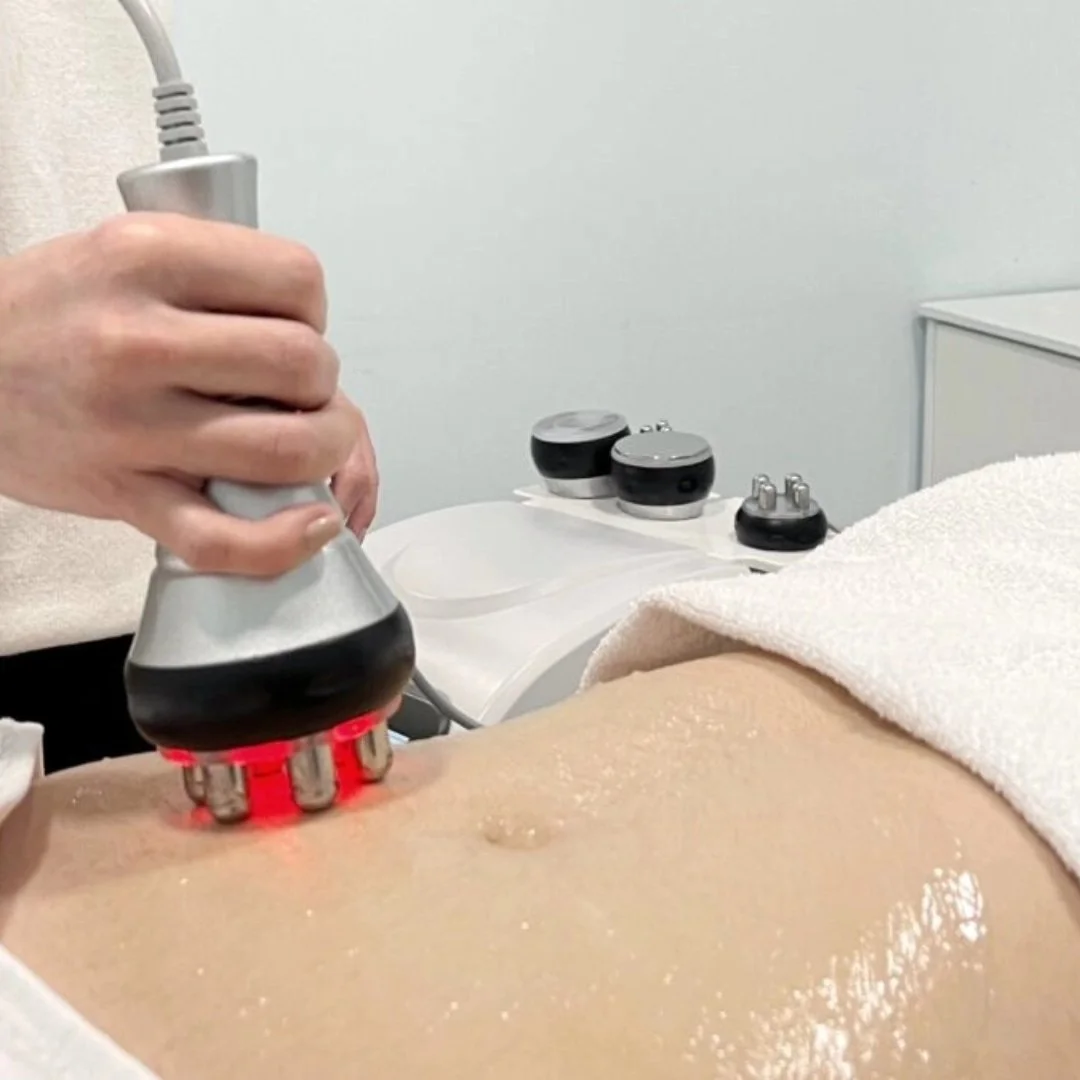 A person receiving a ultrasound therapy treatment on their abdomen, using a handheld device emitting red light, in a medical setting.