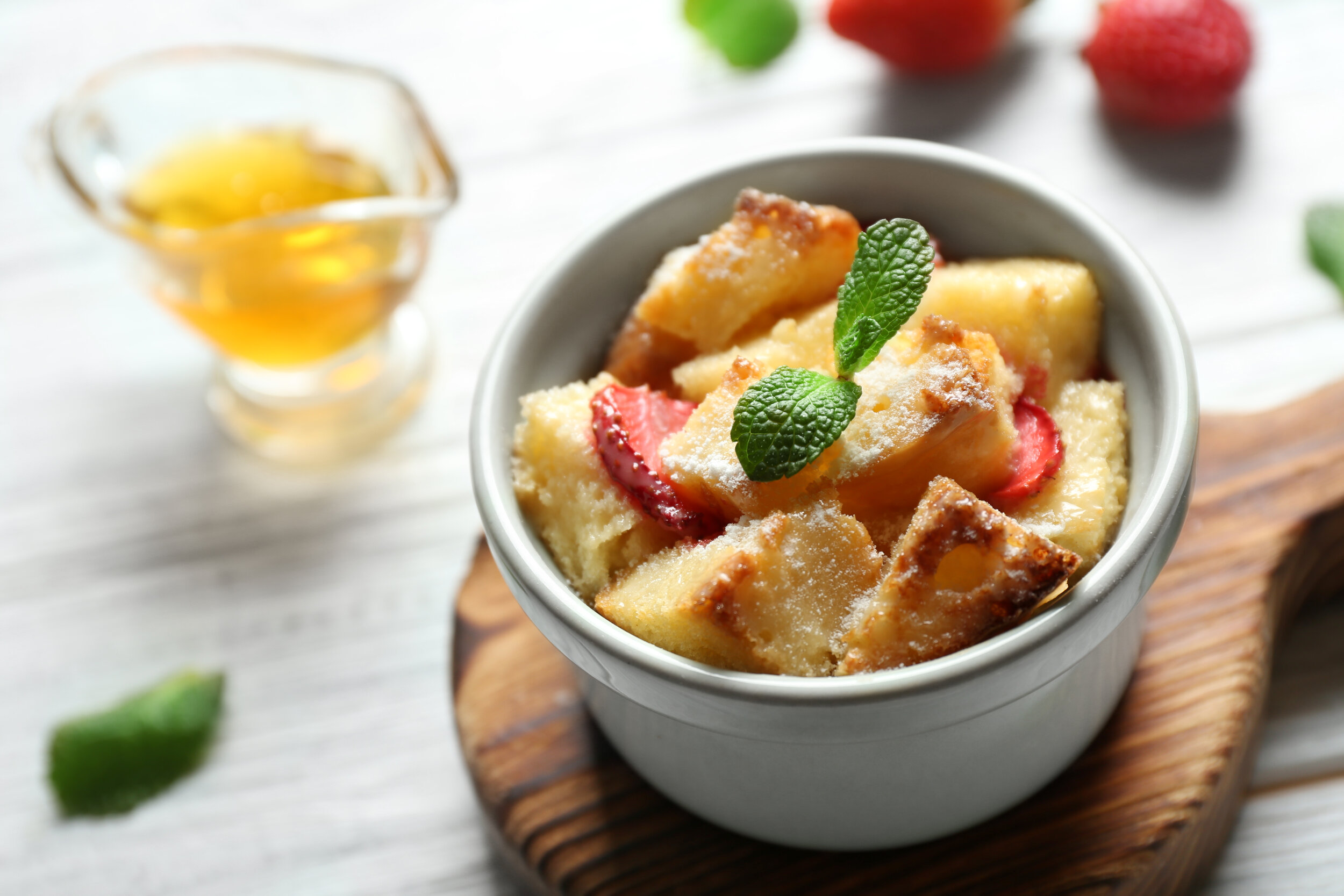 Delicious bread pudding with strawberry and mint in bowl on wooden board