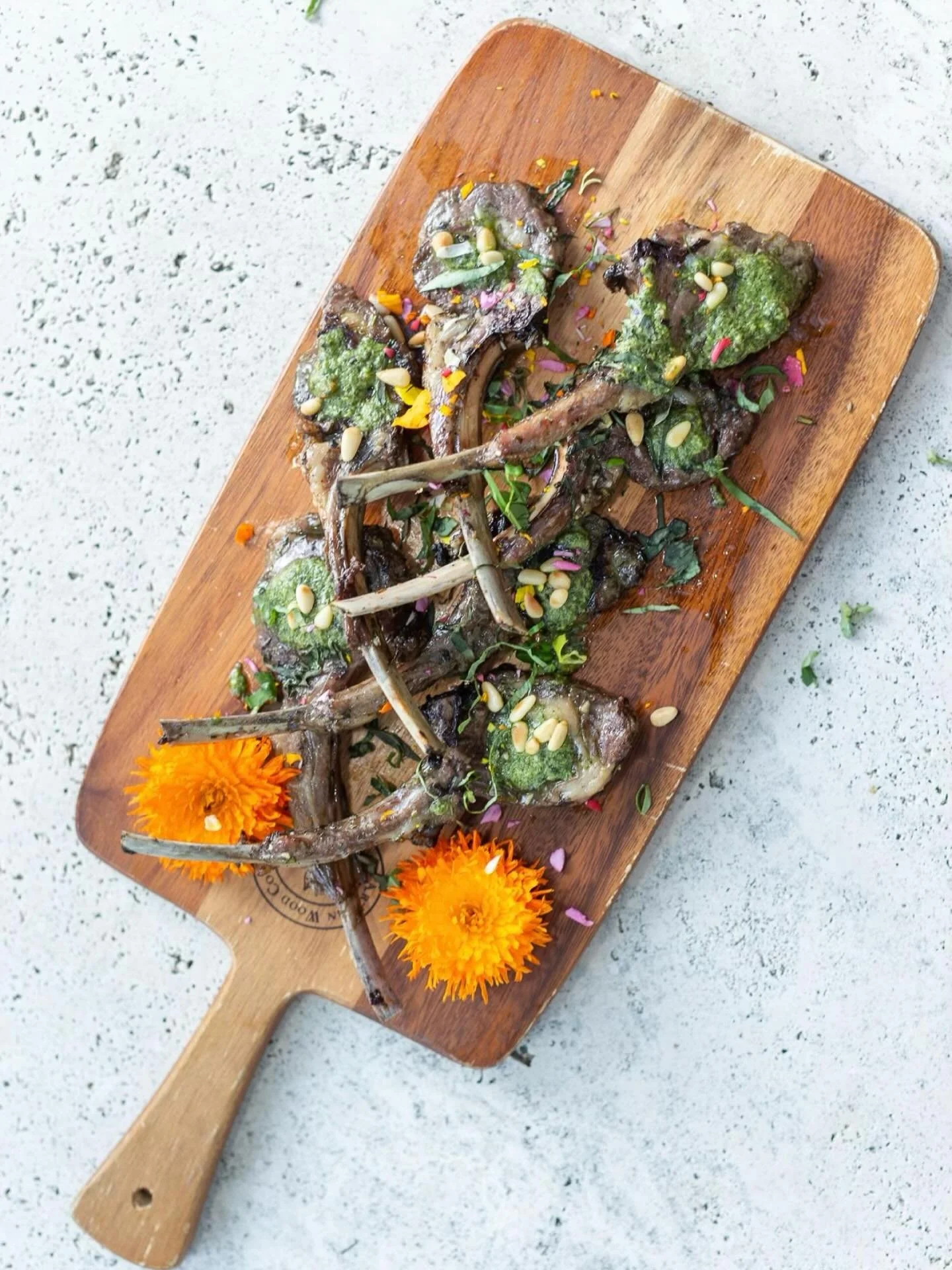 Elegance on the plate &mdash; tender lamb chops complemented by vibrant pesto, toasted pine nuts, and delicate seasonal blooms. ✨ 
Discover more refined small bites in our latest blog post, where we share the perfect appetizers to grace your next din