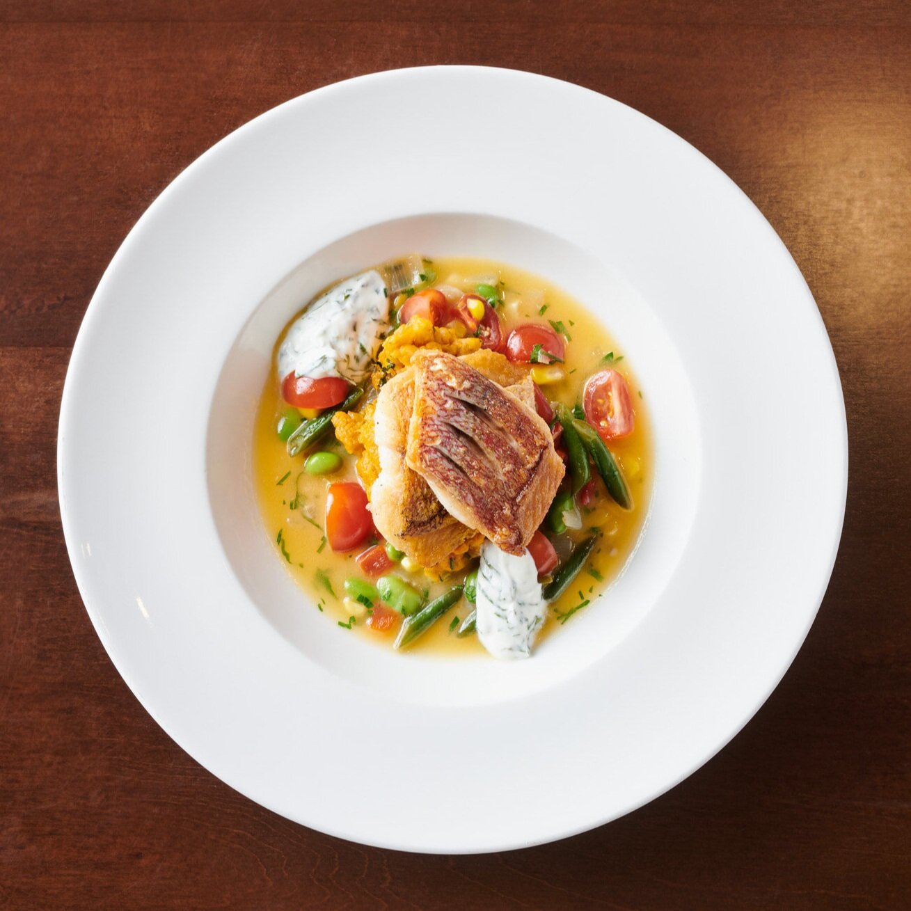 An entrée at The Restaurant of Pan-seared Red Snapper Succotash, Forked Potatoes, Herb Sour Cream (Copy) (Copy)