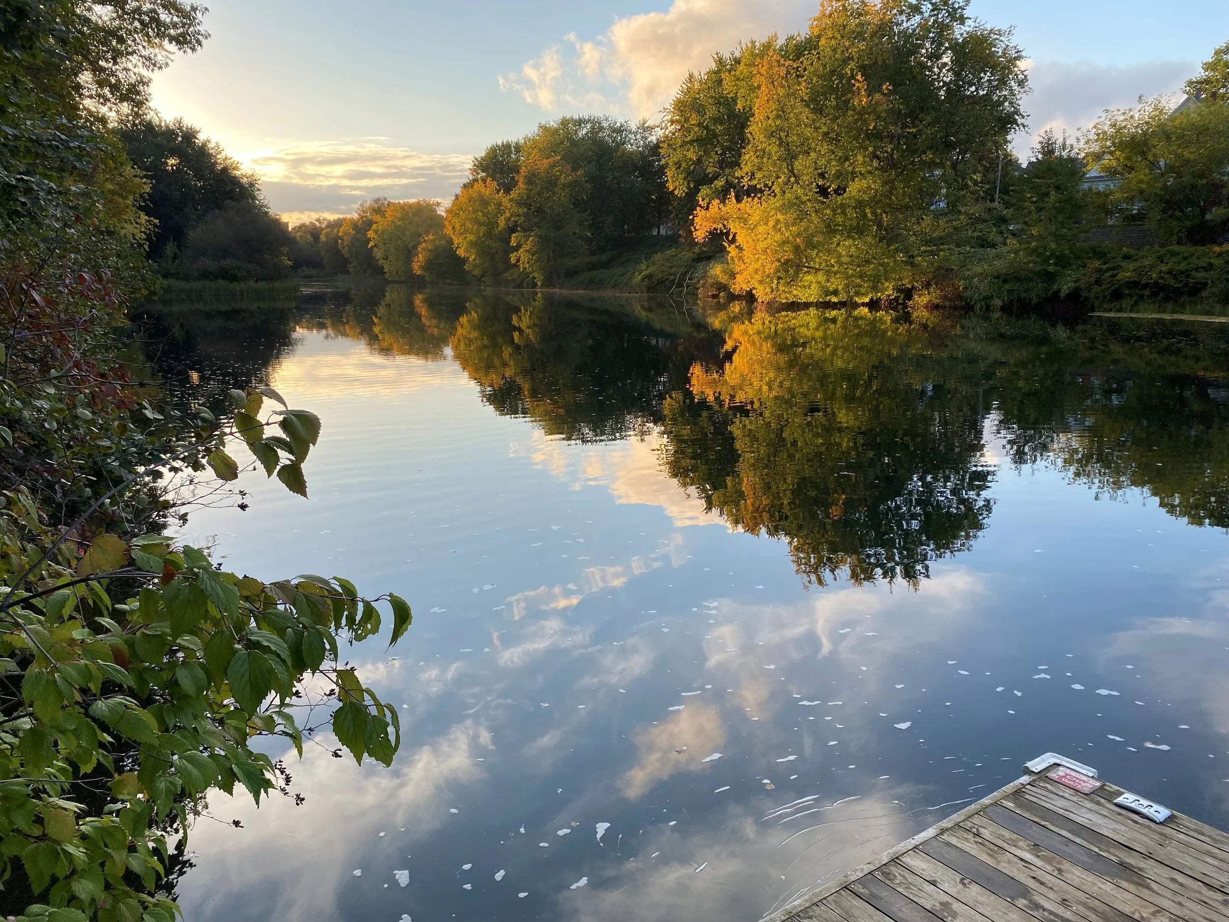 Presumspcot River at sunset as seen from a dock or porch. The river is surrounded by trees which are reflected in the water.