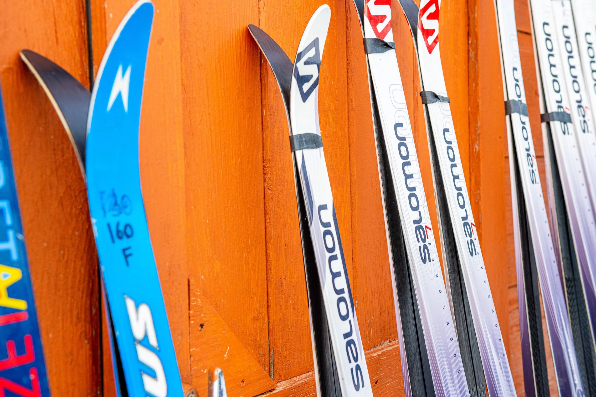 Close up of pairs of skis leaning against an orange wall