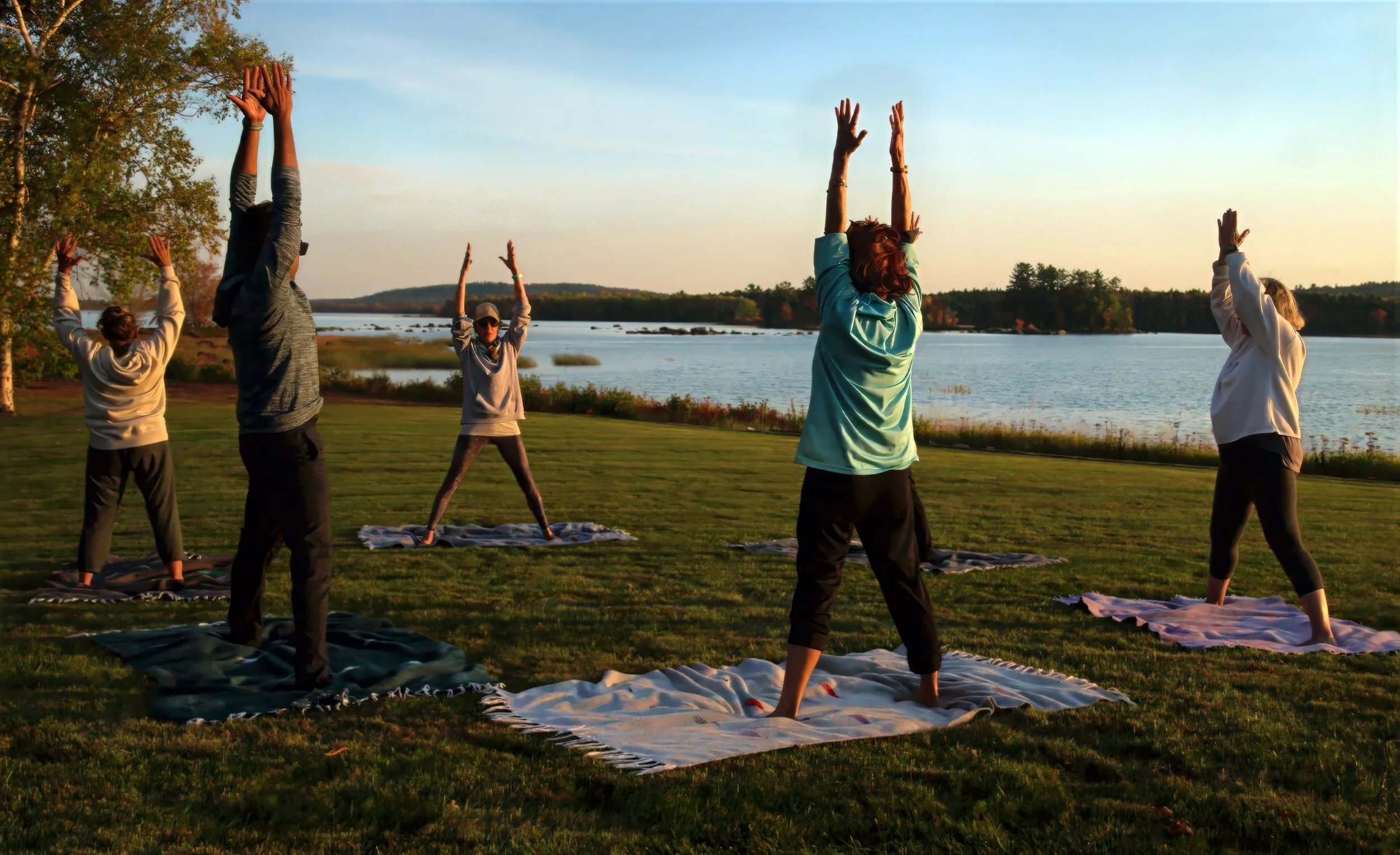 Four students and a yoga teacher do a yoga pose during sunrise or sunset