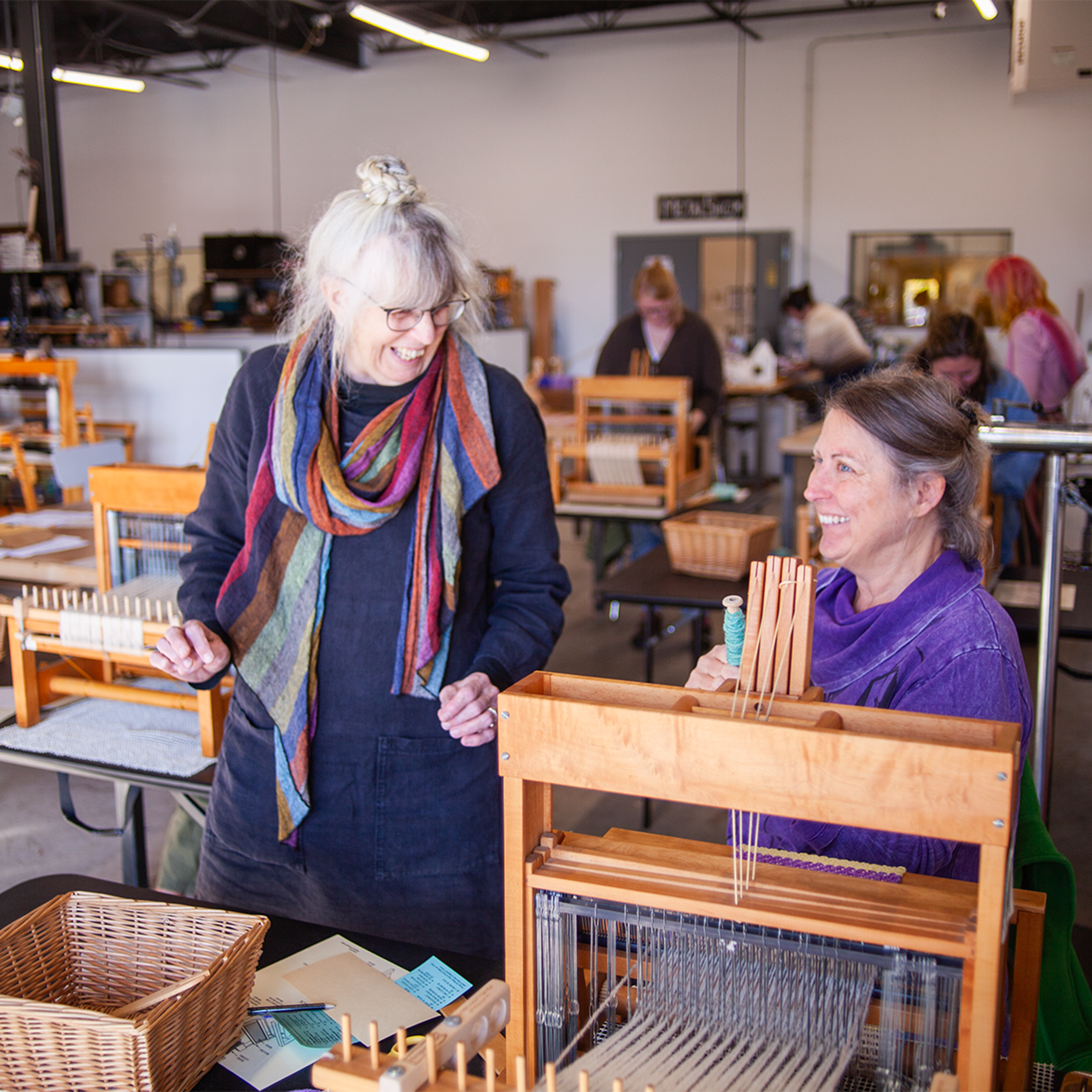 Two women smile over a weaving loom
